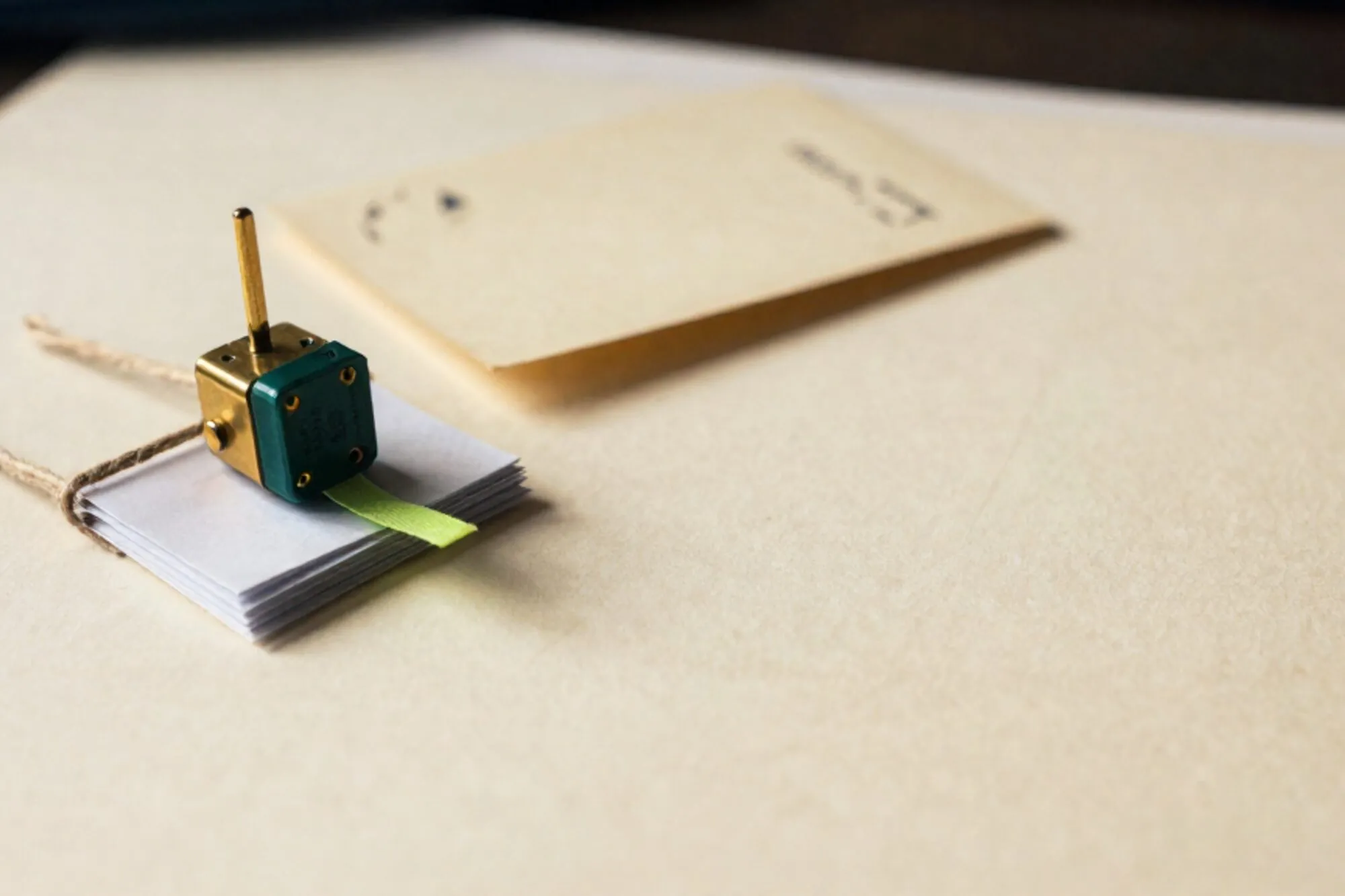 Brass relay switch beside stack of paper slips tied with twine, green ribbon, cream index card on ivory surface.
