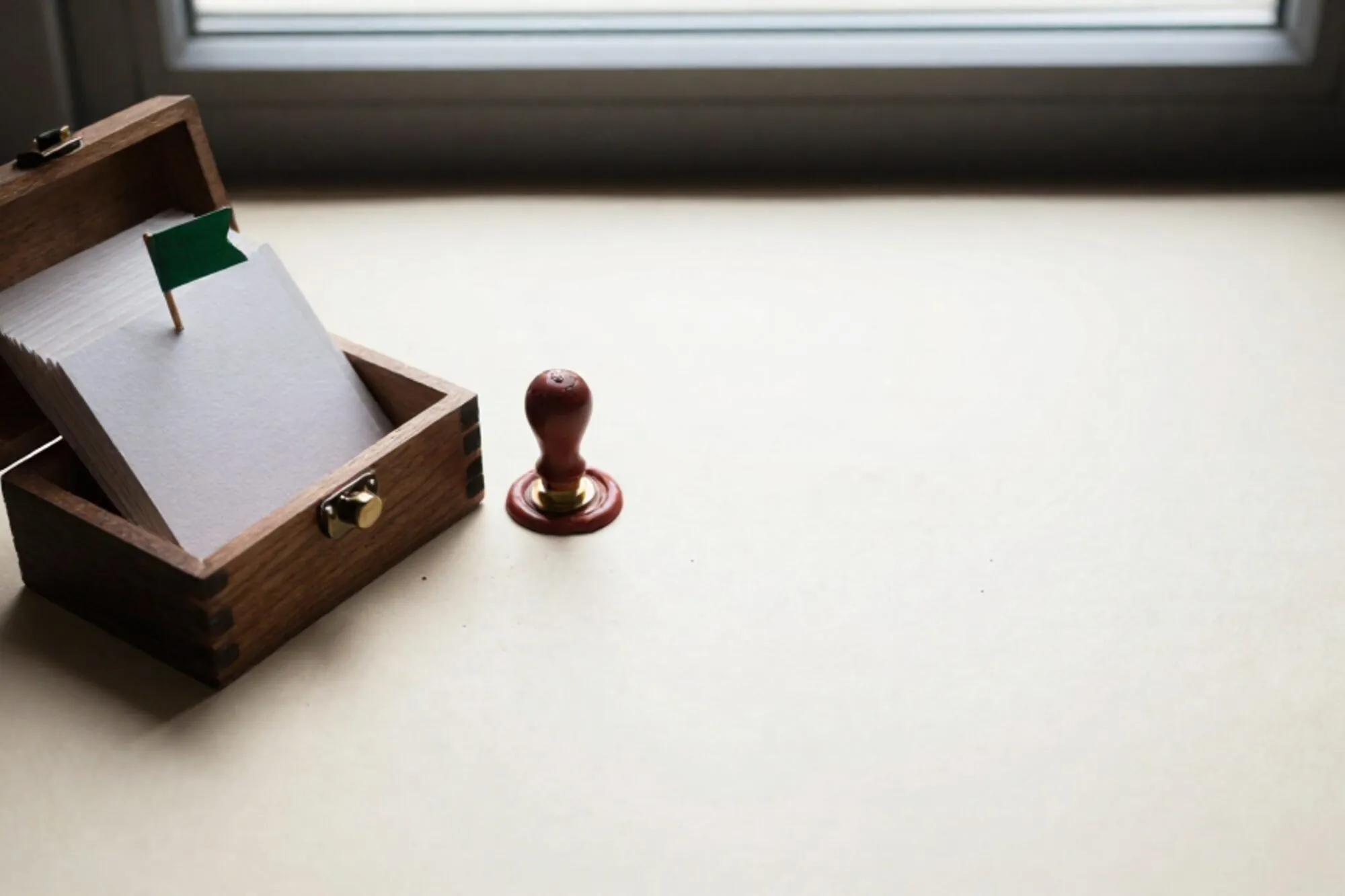 Open wooden card-index box on ivory paper, typed cards, green flag pin, brass tab, red wax seal, soft window light.
