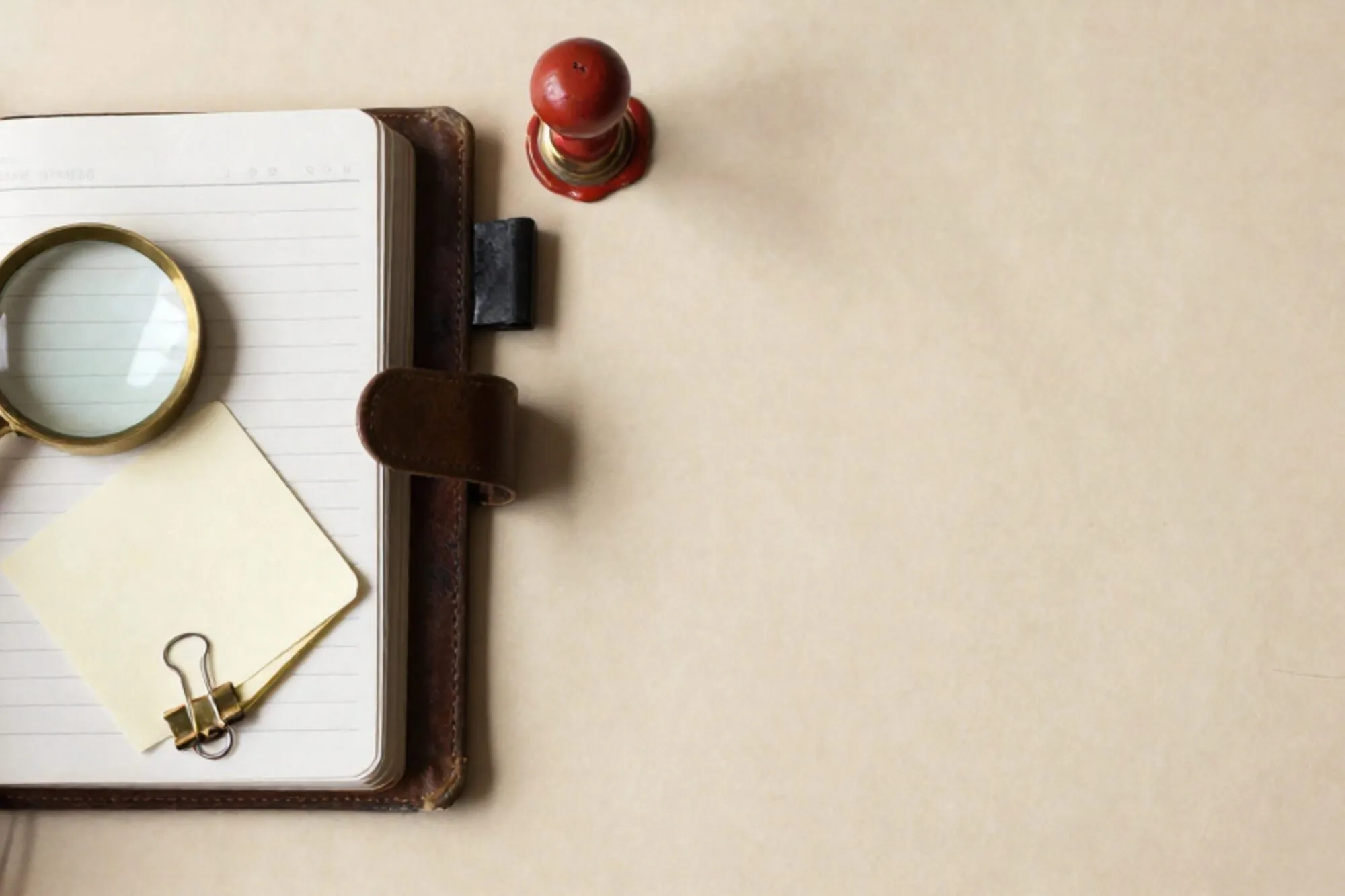 Open leather ledger with brass magnifier, cream index cards clipped together, green tab marker, red wax seal on ivory paper.