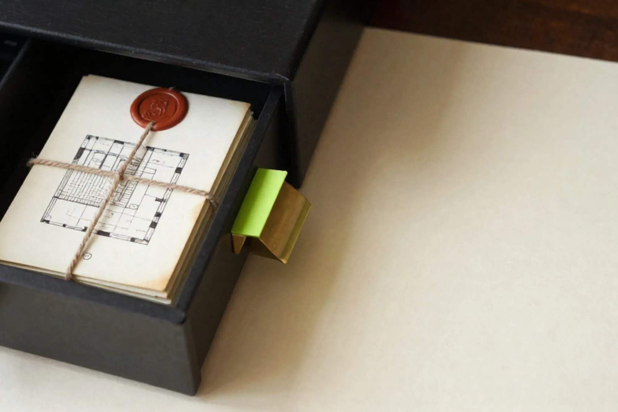 Open wooden index card drawer with floorplan sketch, linen-tied cream cards, green tab marker, red wax seal on ivory paper.