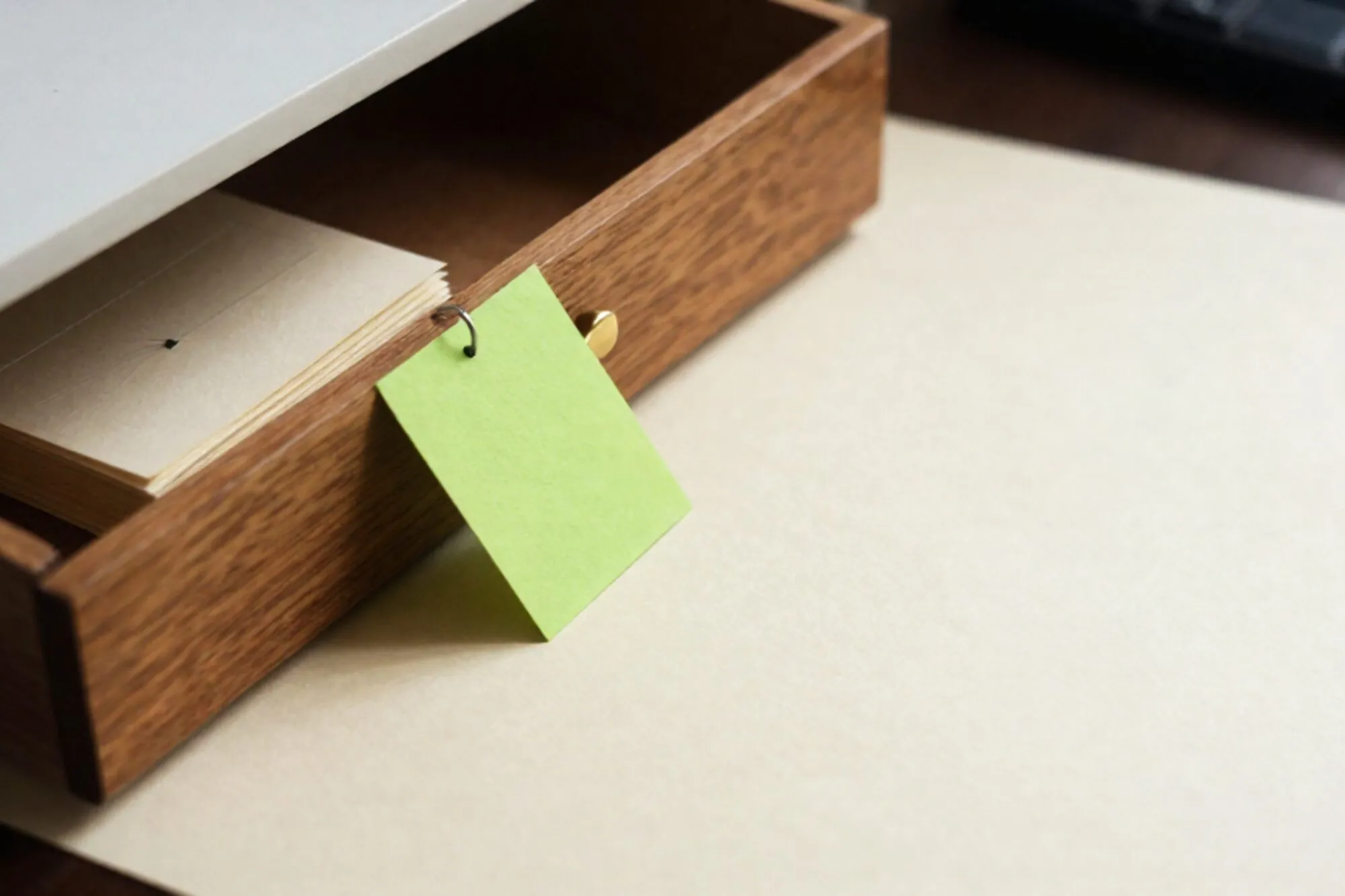 Open eiken kaartenbaklade met één lichtgroene kaart rechtop, stapel crèmekleurige kaarten ernaast, koperen tussenschot, ivoren papier.