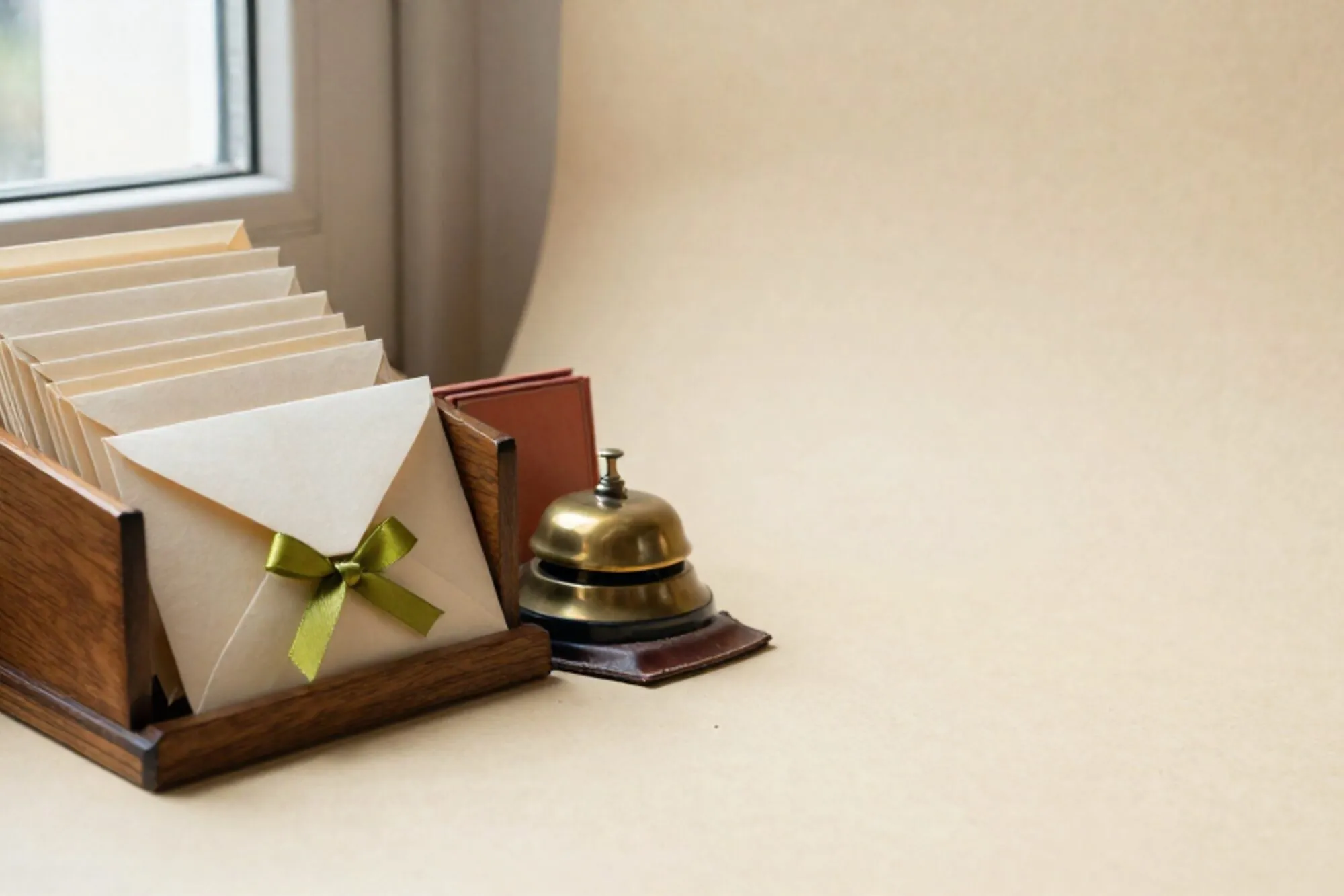 Houten sorteerrek met crème enveloppen op ivoorpapier, één met groen lint, koperen bel en leren vloeiblok ernaast.