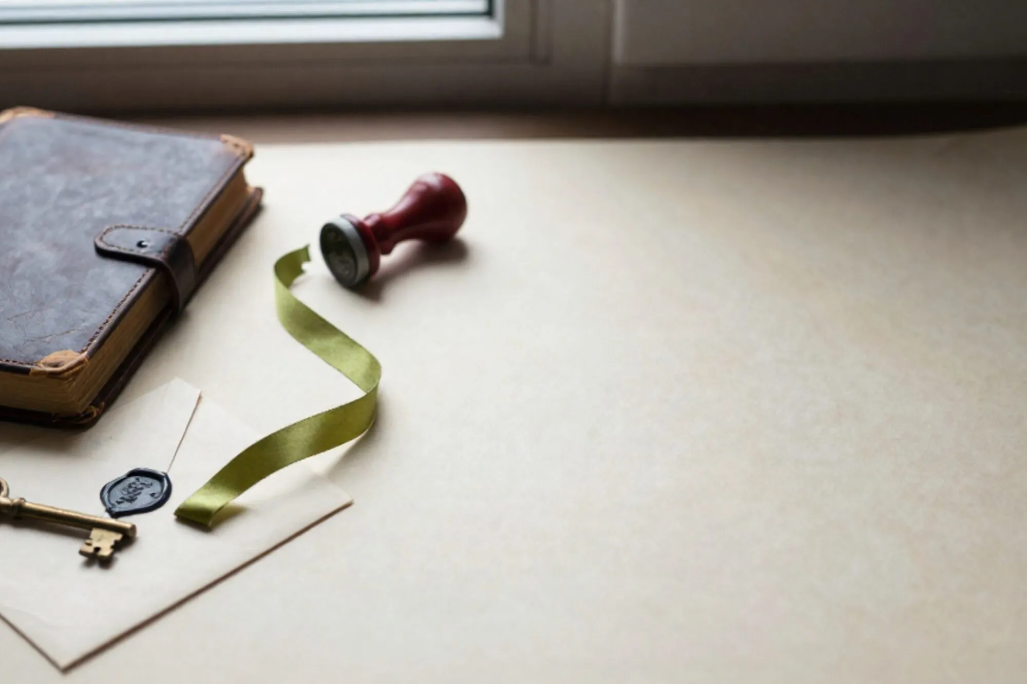Leren logboek, koperen sleutel op crème kaart, verzegelde envelop met groen lint, rode stempel op ivoor papier.