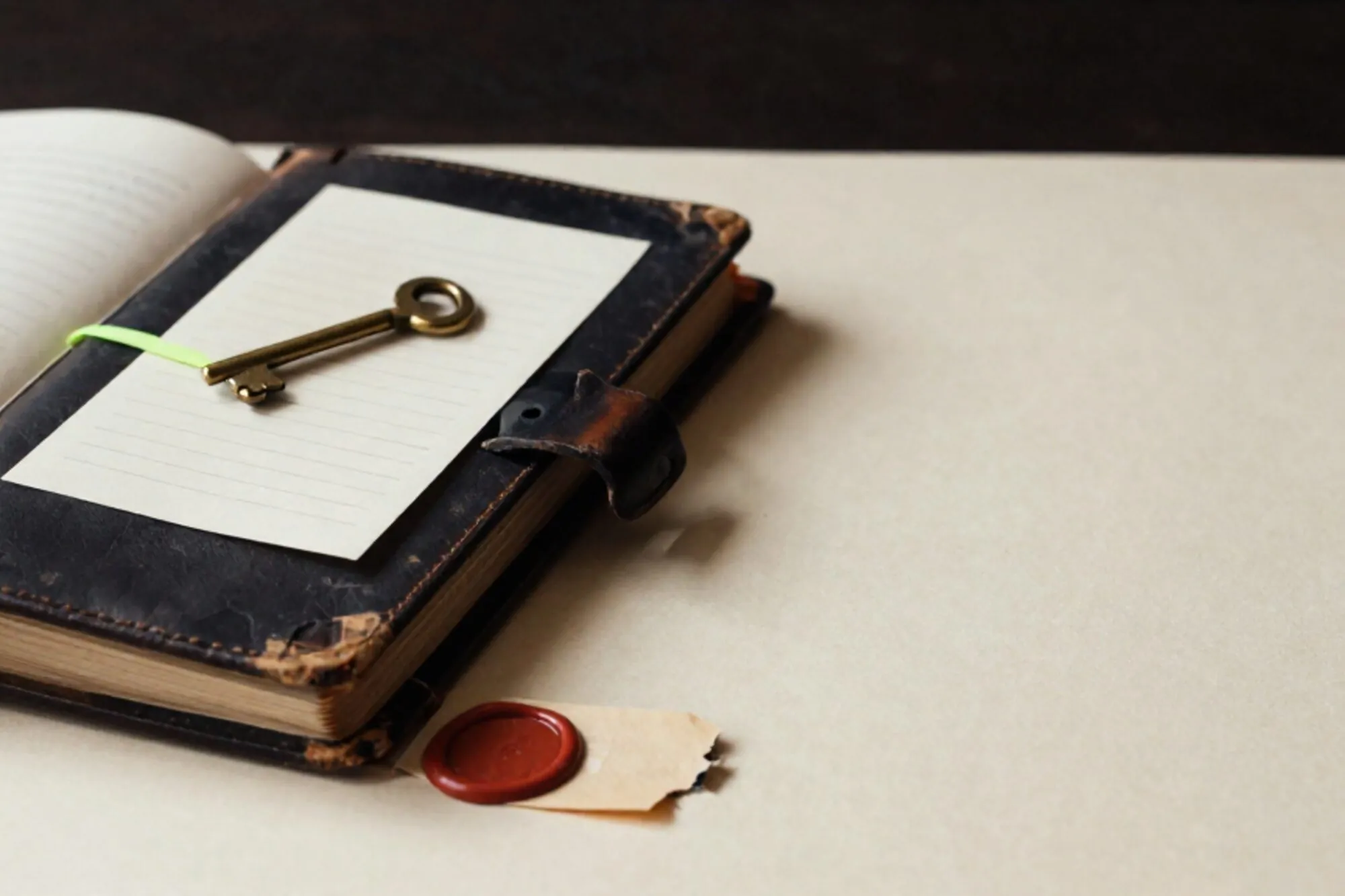 Leather logbook half-open on ivory desk, brass key on cream card, green paper tab, broken red wax seal.