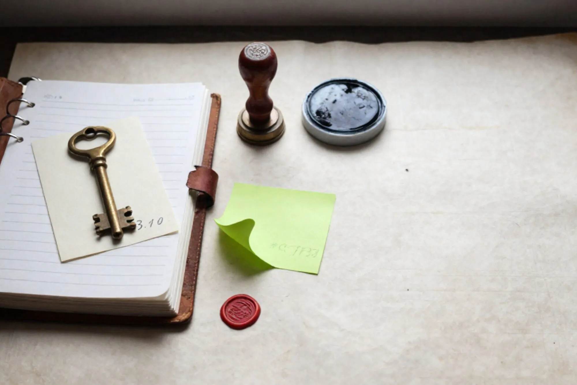 Open leather logbook, two brass keys on index cards marked 3.10 and 4.4, green sticky note, red wax seal on ivory linen desk.