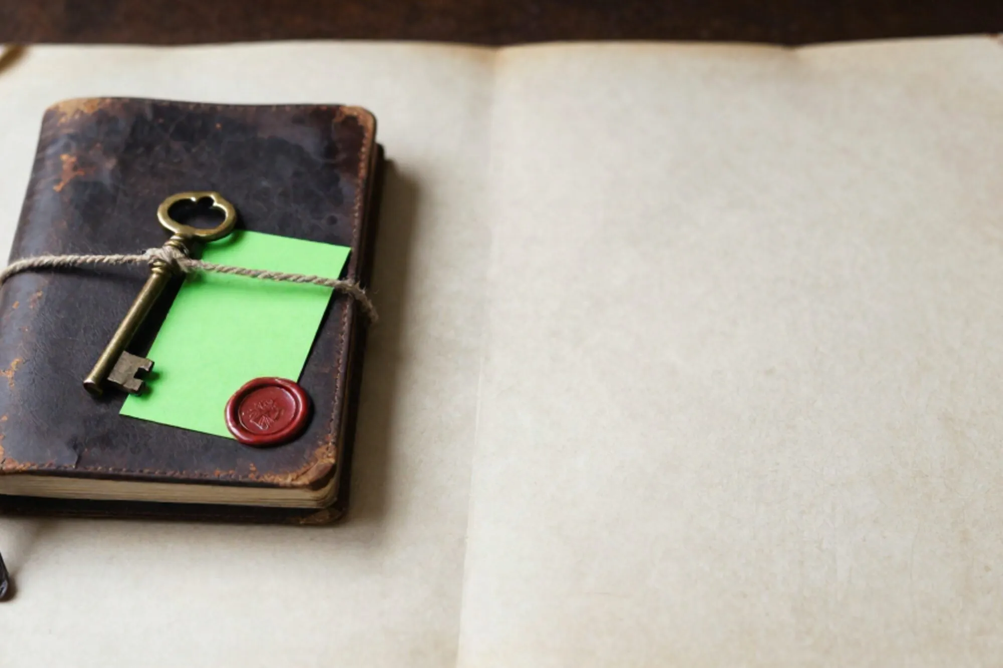 Closed leather logbook with brass key on twine, green index card marker, red wax seal on bone paper desk.