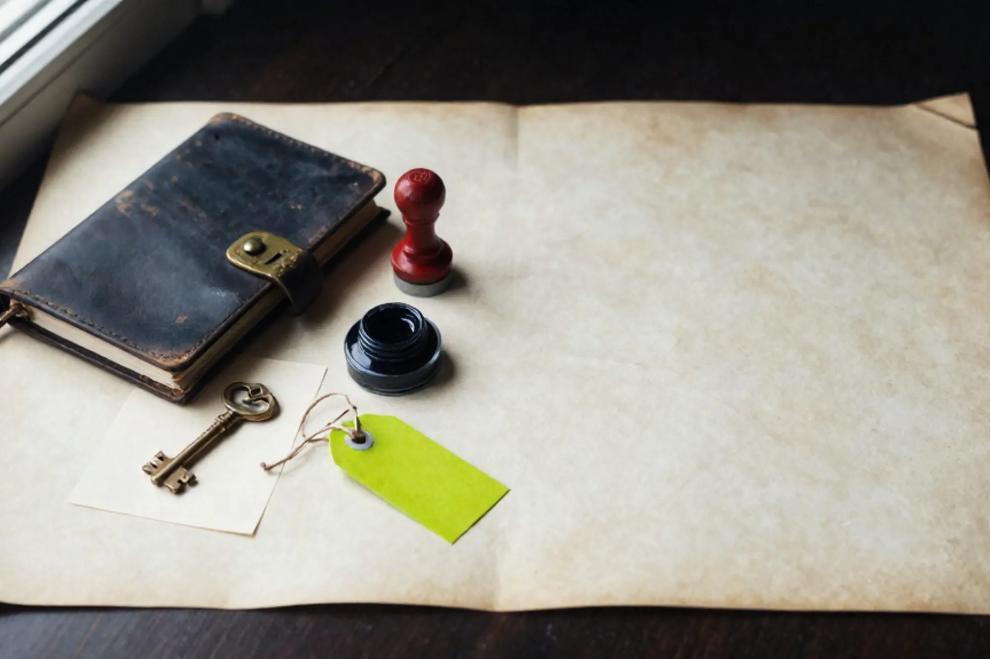 Closed leather logbook with brass clasp, brass key on index card, red date stamp, ink pad, green paper tag on ivory blotter.