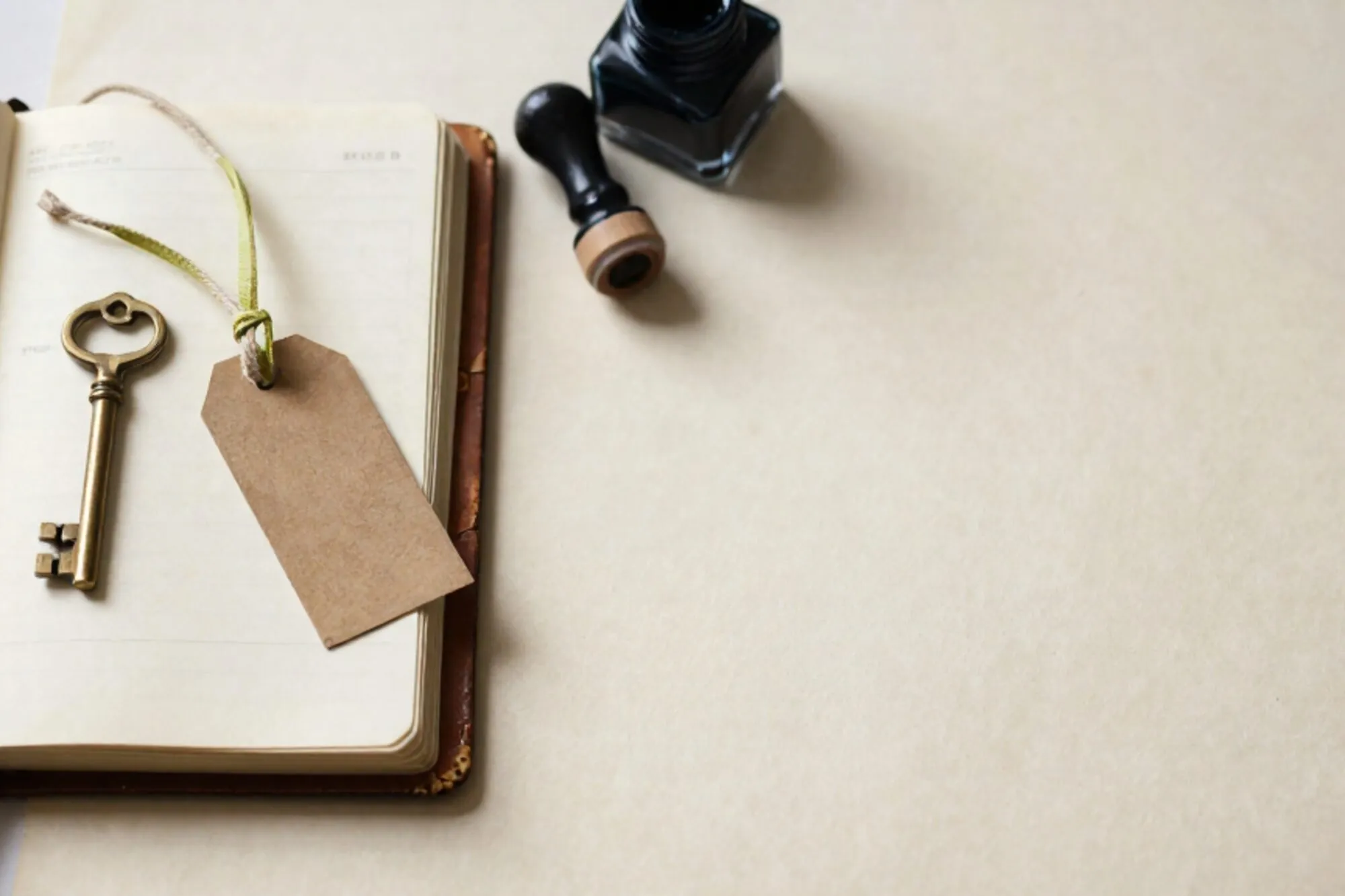 Open leather logbook, brass key on cream card, frayed shipping tag with green ribbon, ink pad on ivory paper.