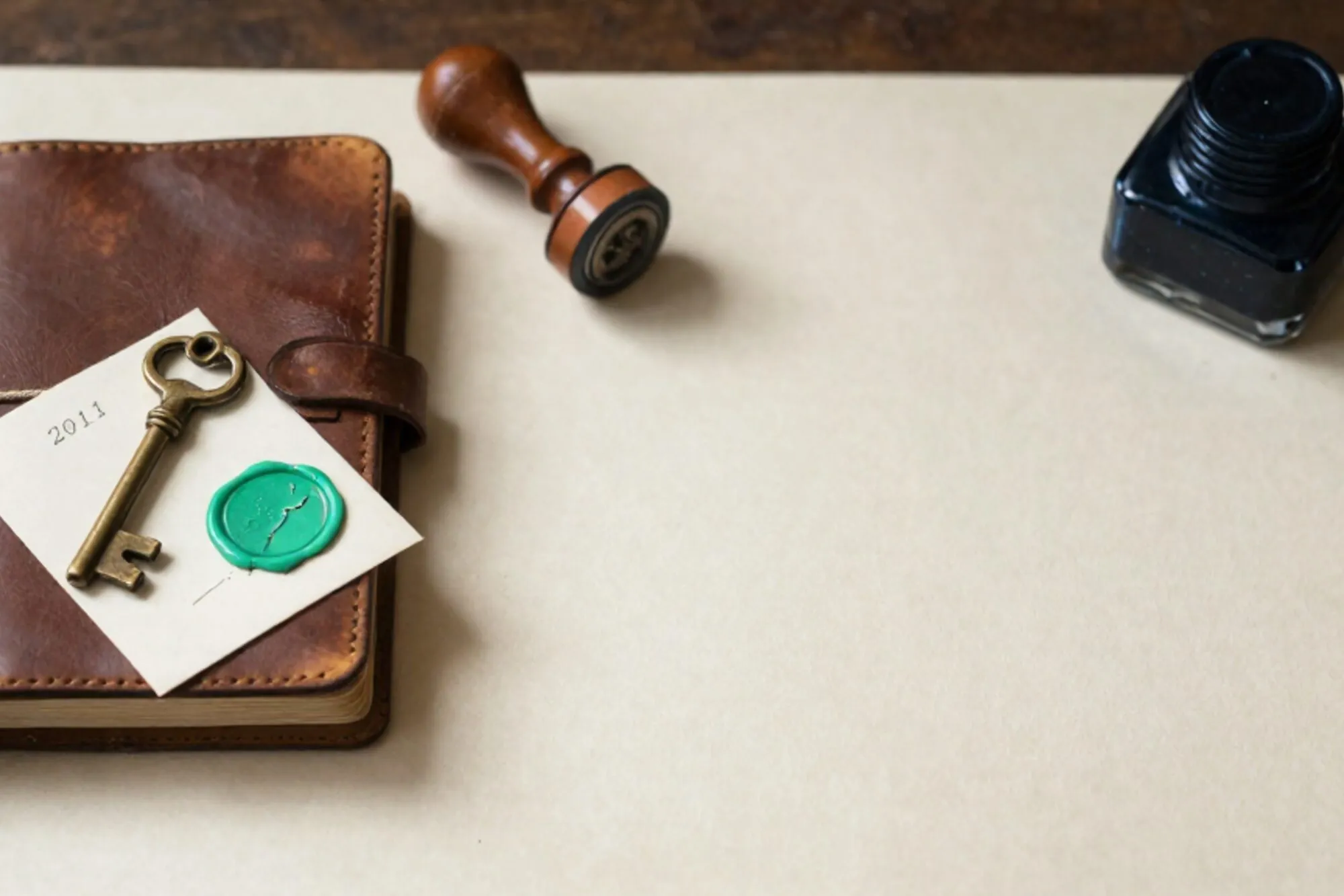 Leather logbook tied with linen ribbon, brass key on a 2011 index card, cracked green wax seal, rubber stamp, ink pad.