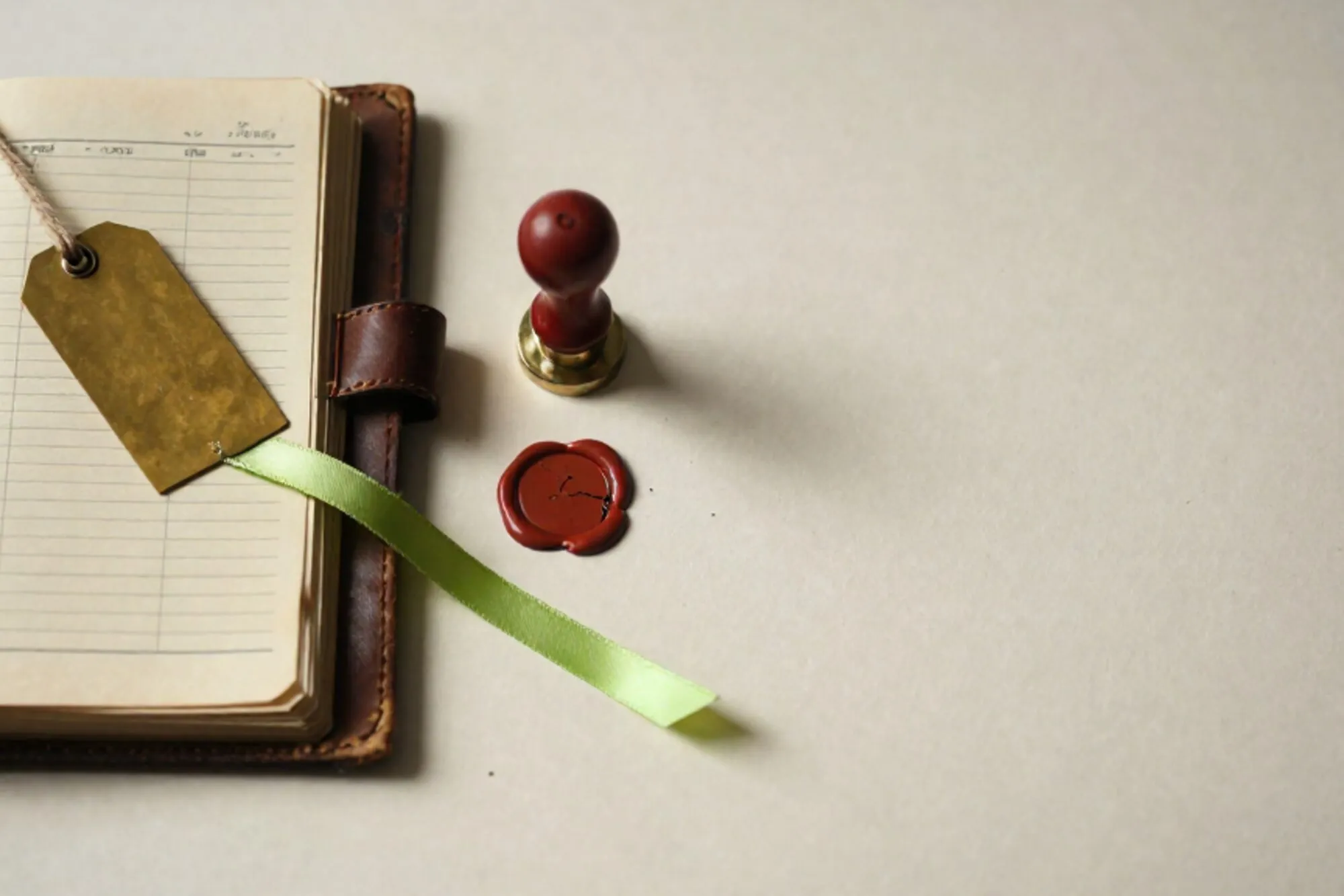 Open leather ledger with yellowed price columns, brass tag on twine, green silk ribbon bookmark, cracked red wax seal on ivory paper.
