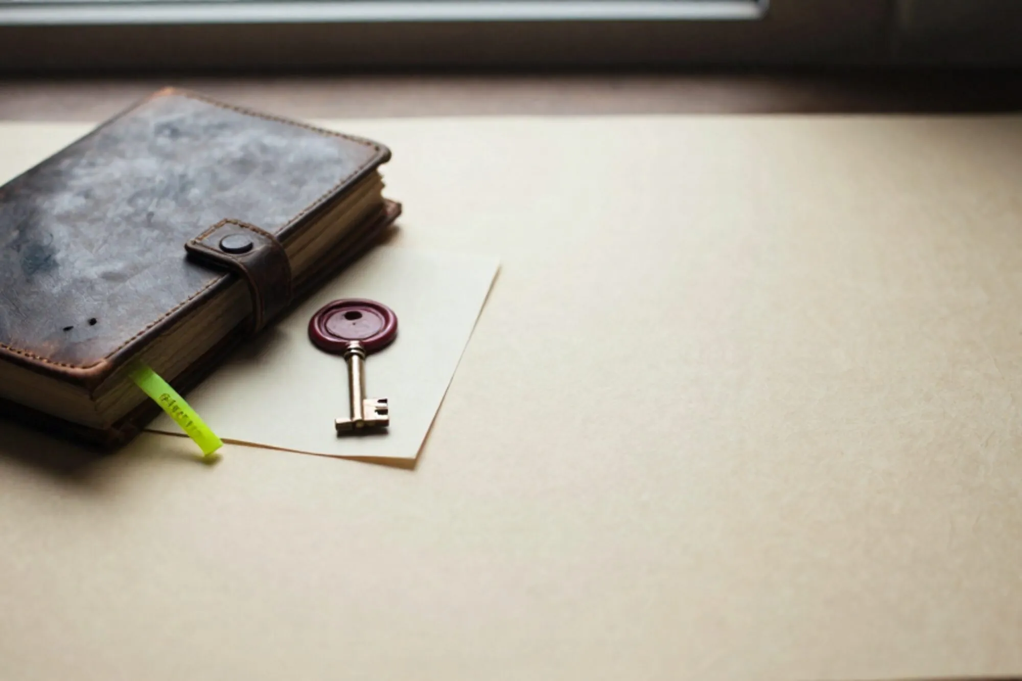 Open leather logbook, brass key on cream card, green ribbon, red wax seal on ivory paper in side light.