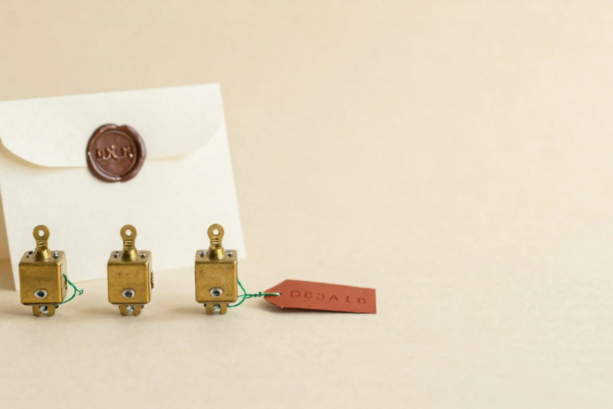 Three brass relay switches on ivory paper, green thread on one, cream card with wax seal, red paper tag.