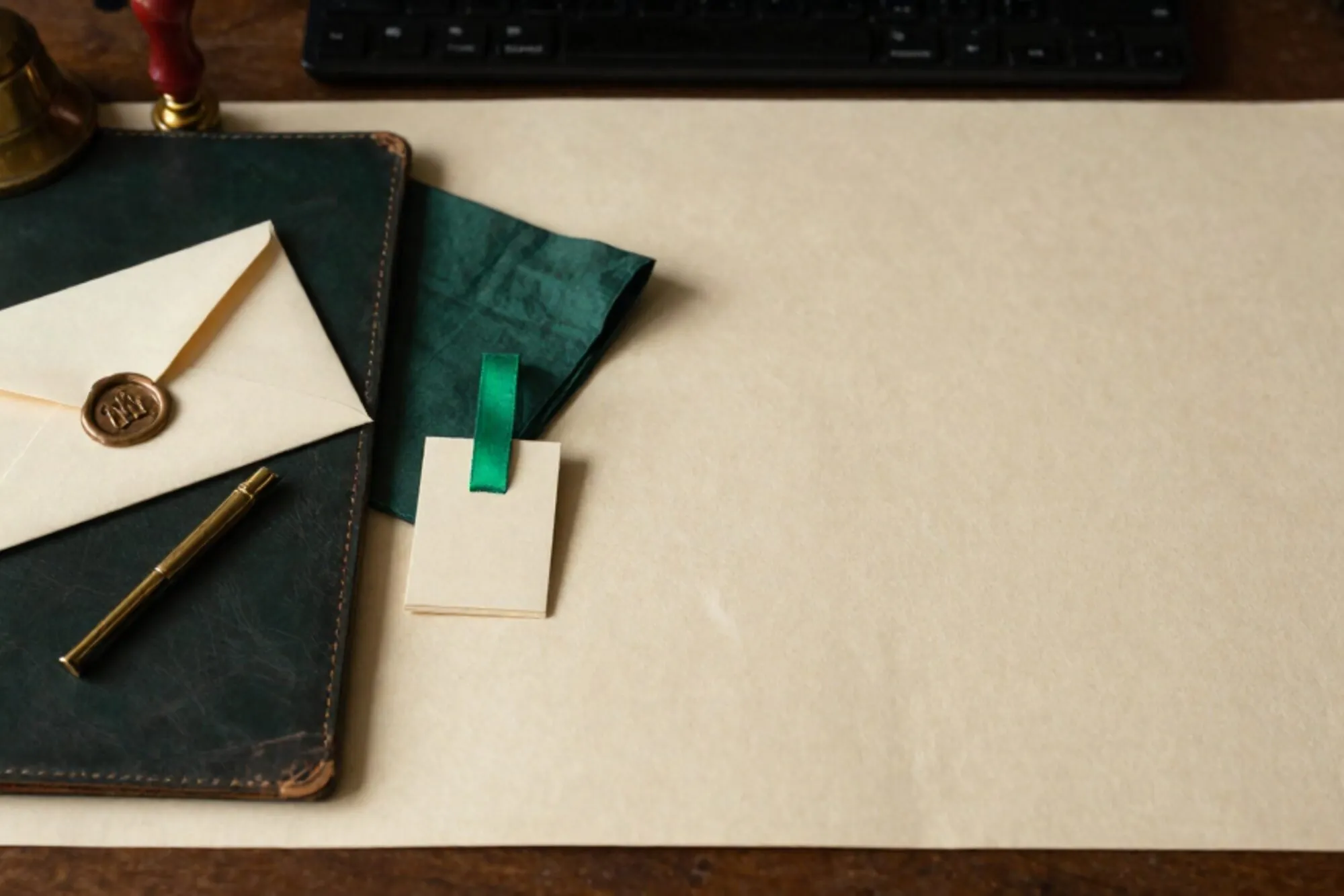 Cream wax-sealed envelope, brass letter-opener, forest pocket-square, ivory card with green ribbon, brass bell on ivory desk.