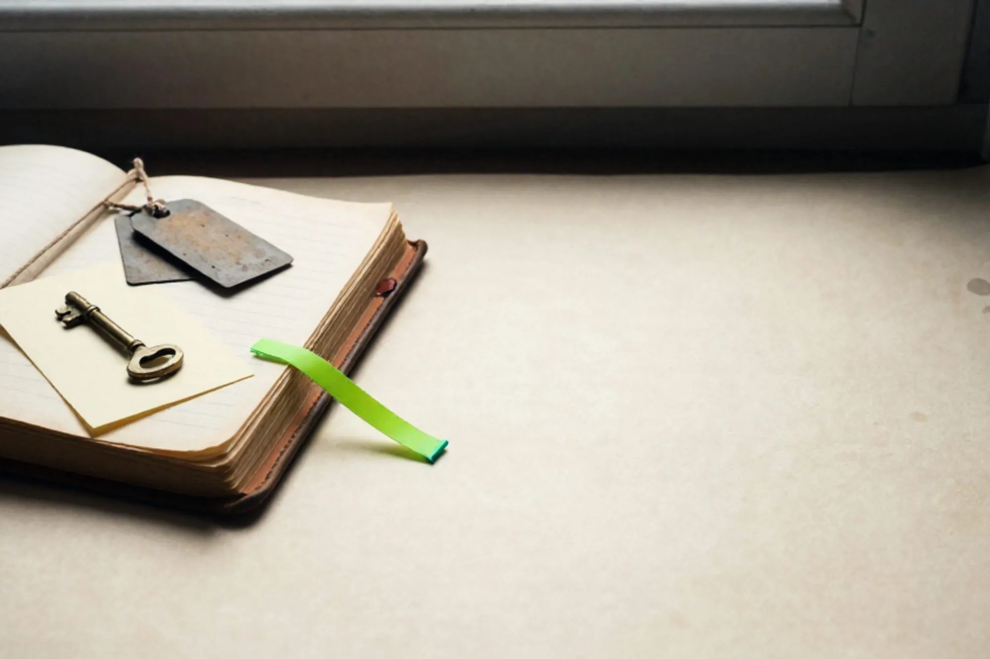 Open leather ledger with linen-tied iron tags, brass key, cream card, green ribbon, red wax fragment on ivory.