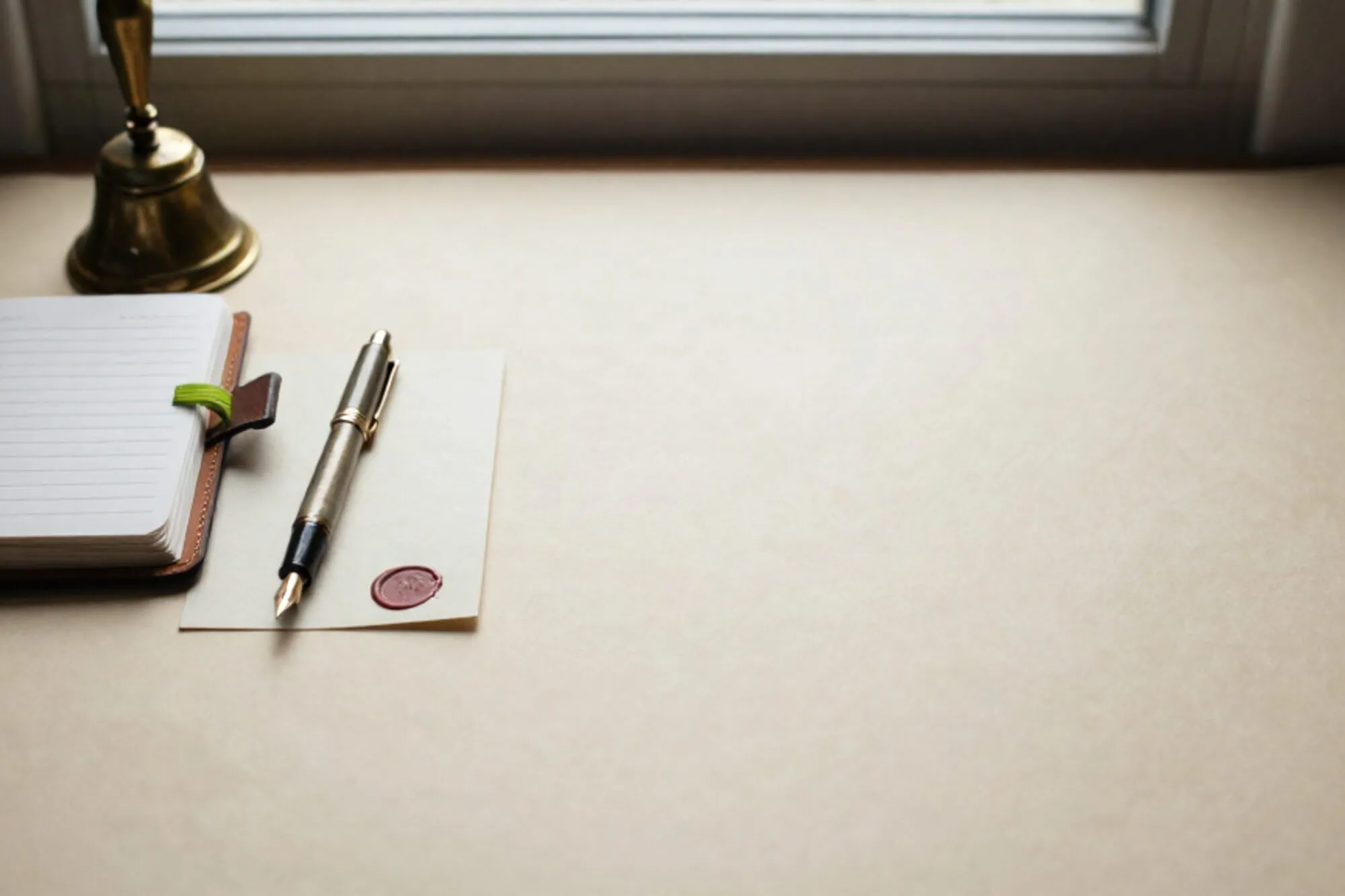 Leather appointment book, brass bell, green ribbon, fountain pen on index card, red wax seal on ivory desk.