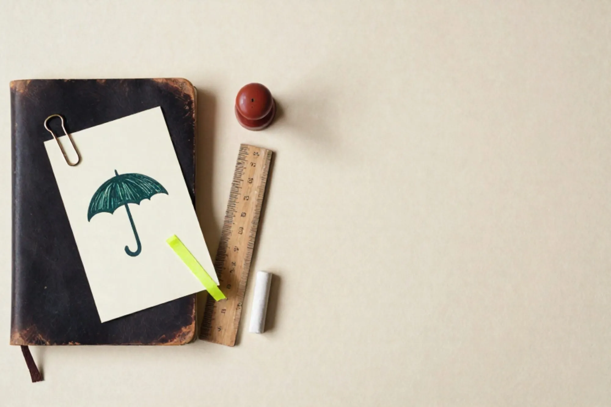 Leather notebook, cream index card with umbrella symbol, brass clip, green ribbon, wooden ruler, chalk, red wax seal.