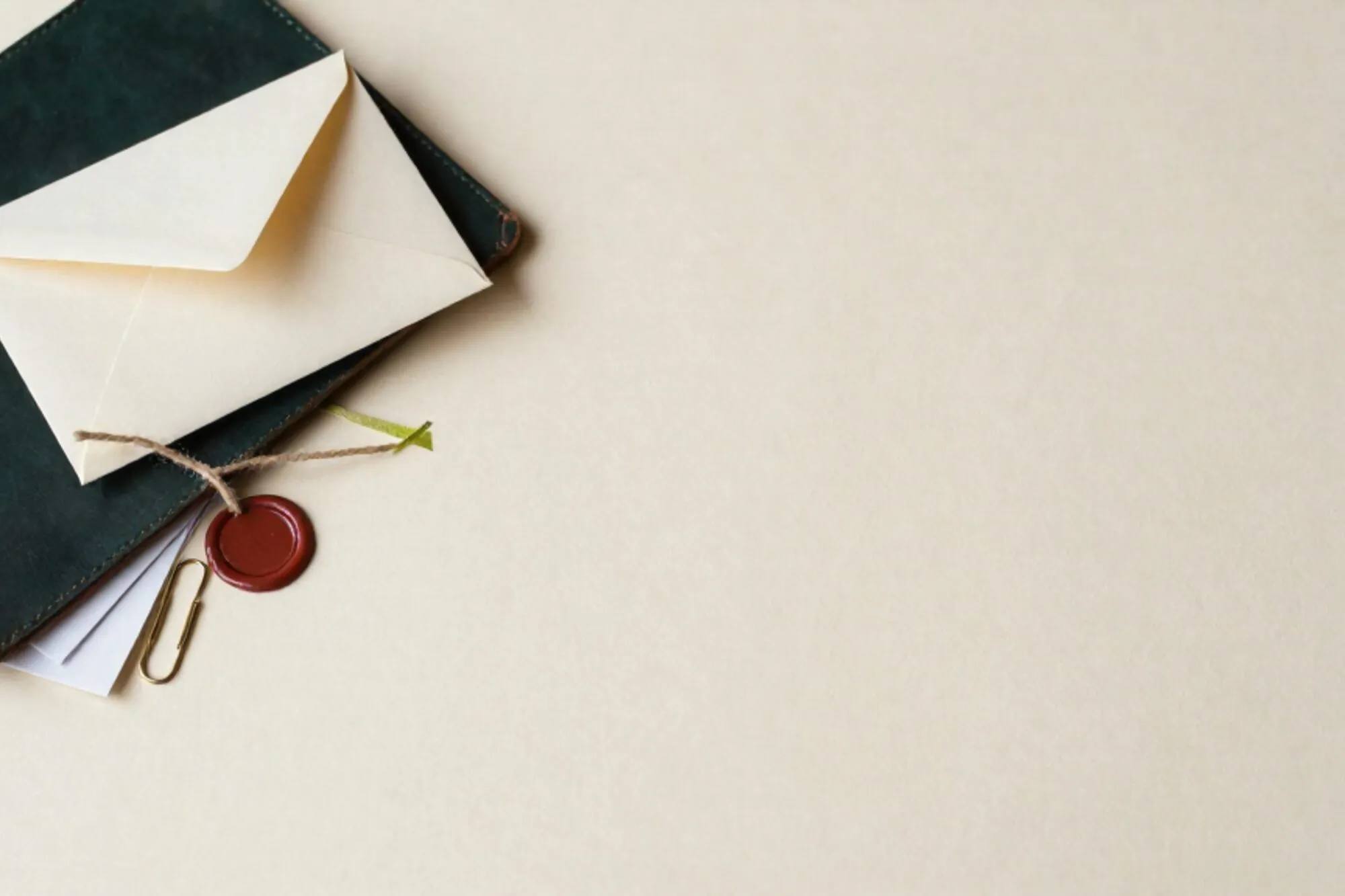 Cream envelope tied with green ribbon on dark leather blotter, clipped letters and brass clip on ivory paper.