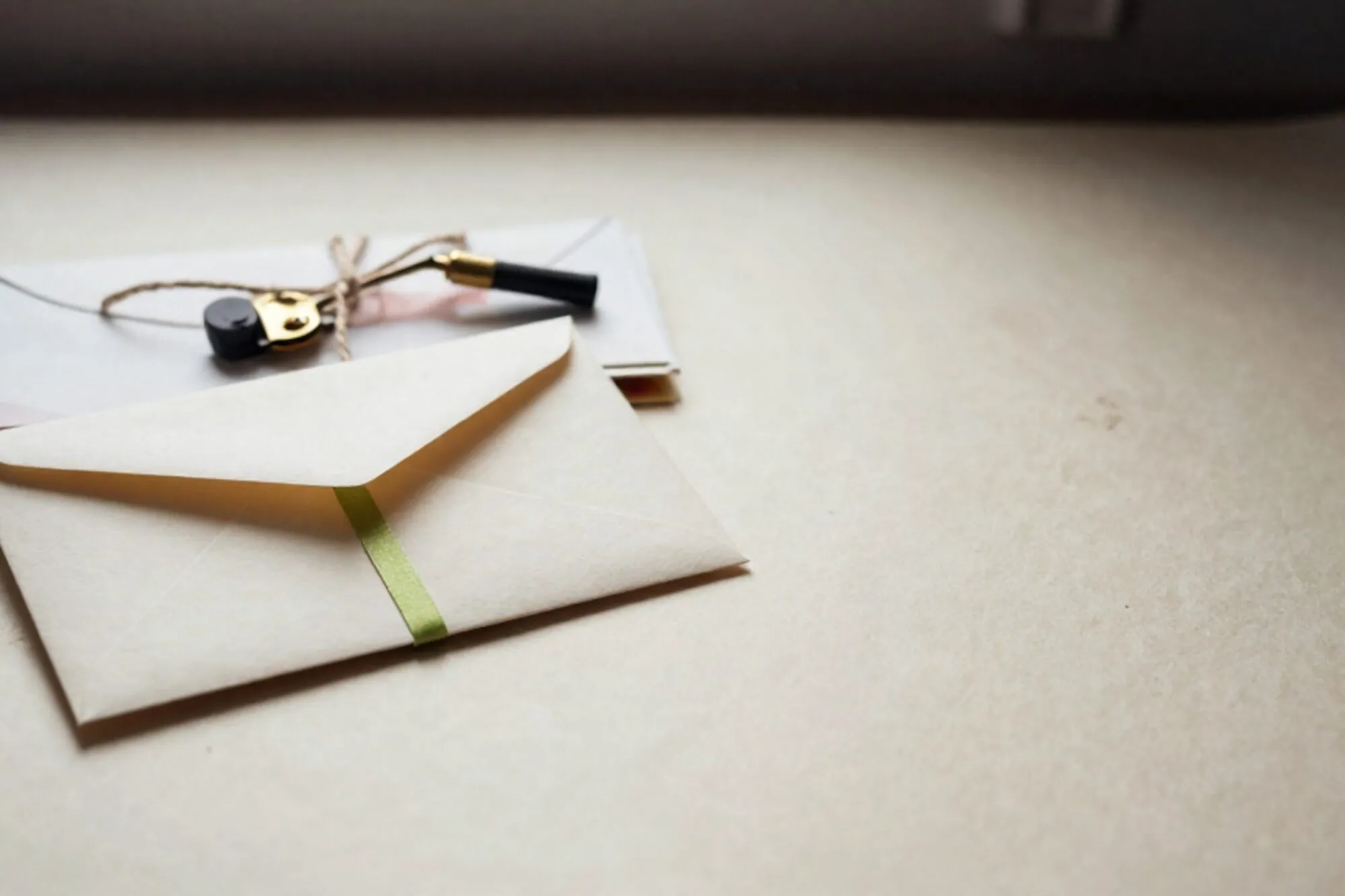 Sealed cream envelope with chartreuse ribbon on a forest-green blotter, stack of letters tied with twine, brass letter opener.