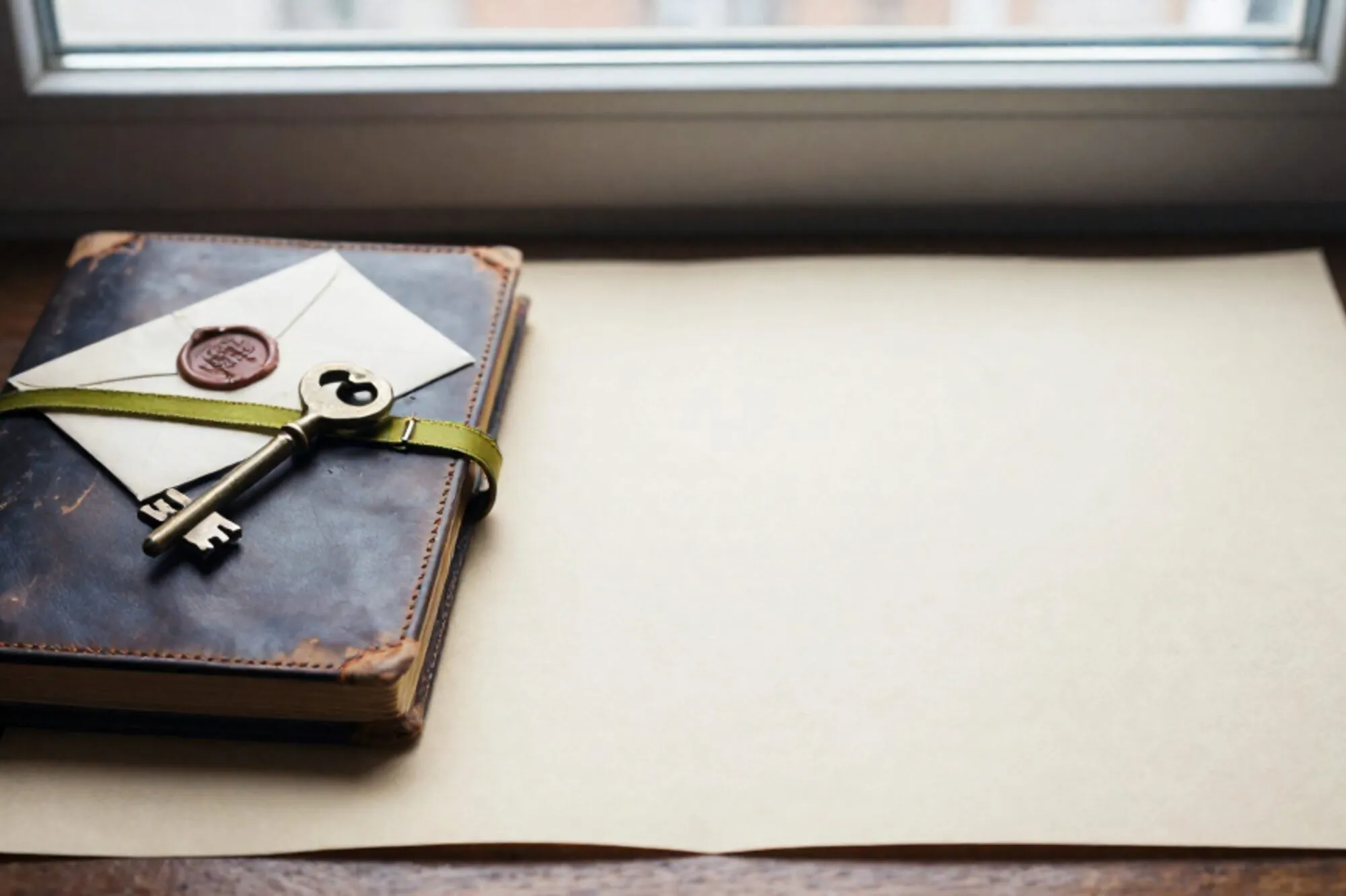 Leren grootboek met messing slot, messing sleutel aan groen lint, gelakte envelop op ivoren bureau bij raam.