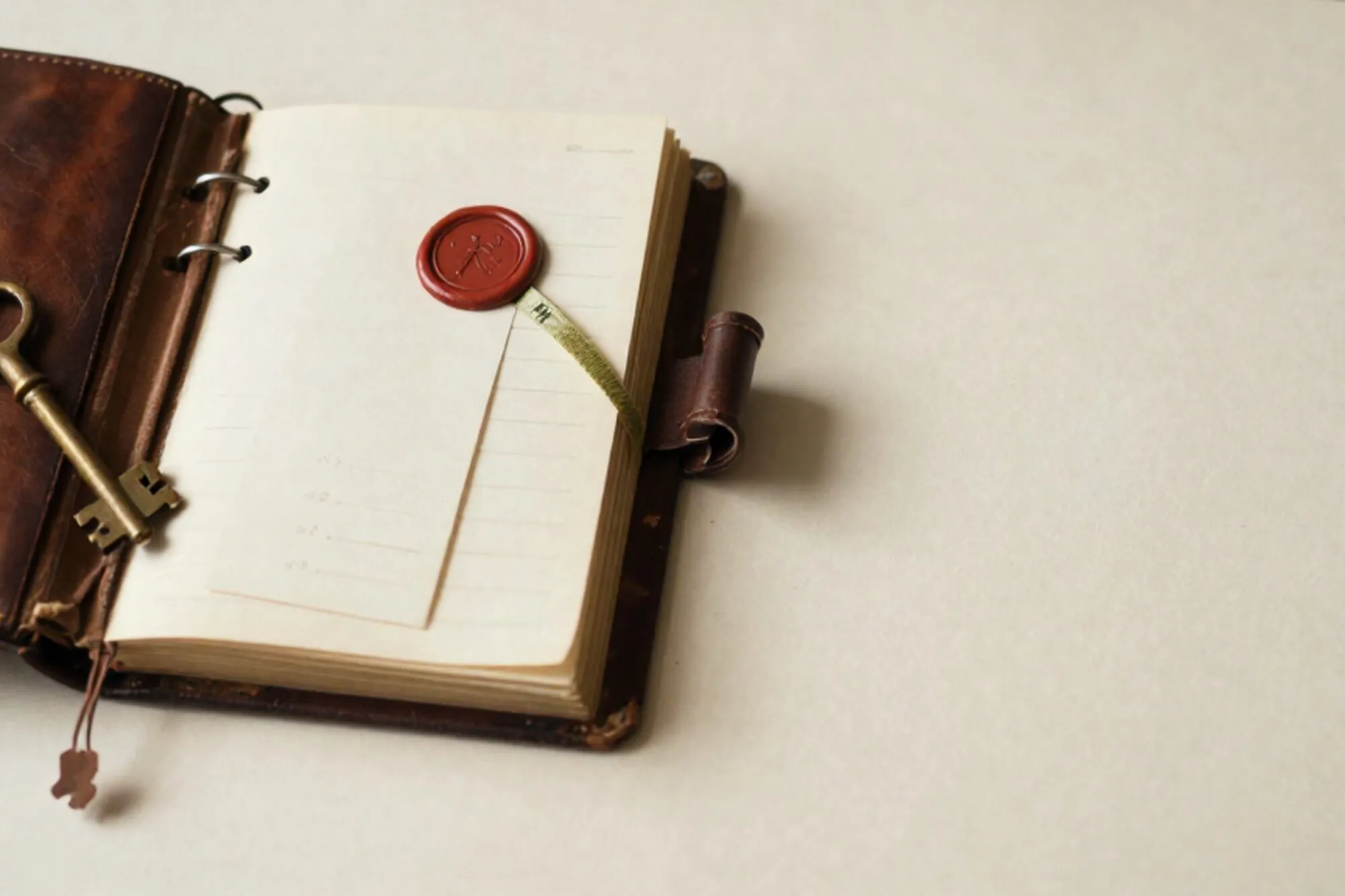 Open leather ledger with brass key on spine, cream index card with green ribbon and red wax seal on ivory paper.