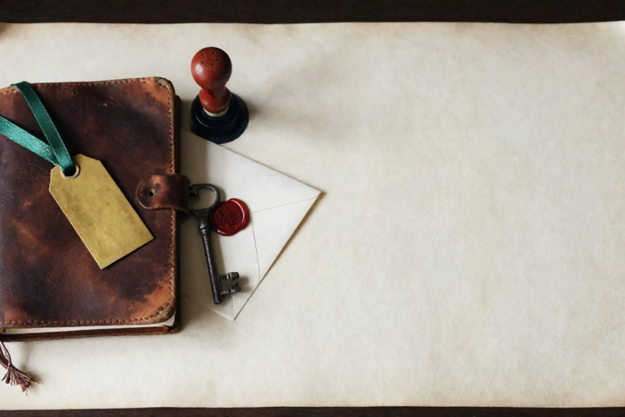 Closed leather ledger with linen tie, brass tag with green ribbon, iron key, wax-sealed envelope, red stamp on ivory paper.