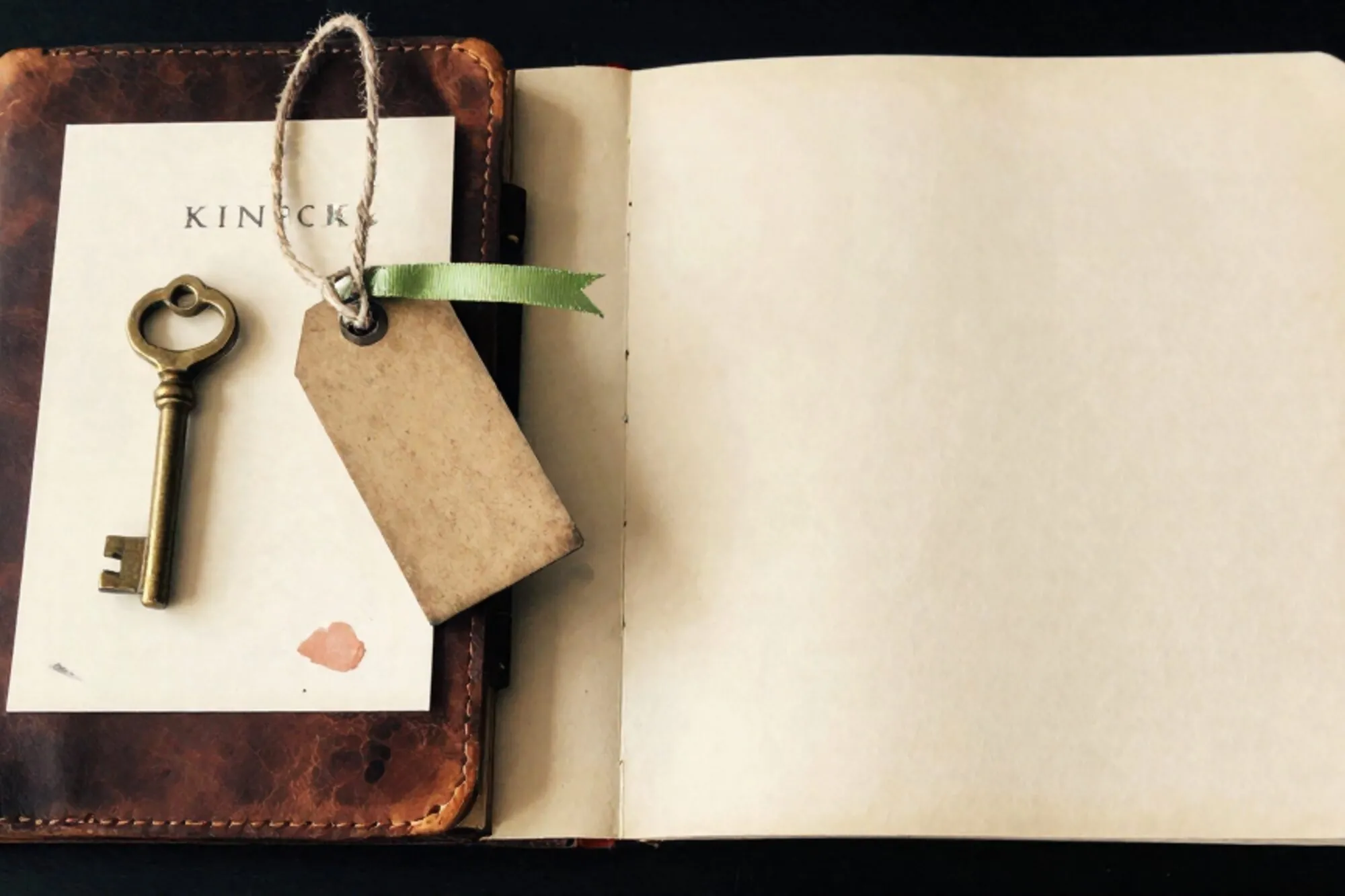 Leather logbook, brass key on cream card, iron tag with chartreuse ribbon and red wax fragment on ivory paper.