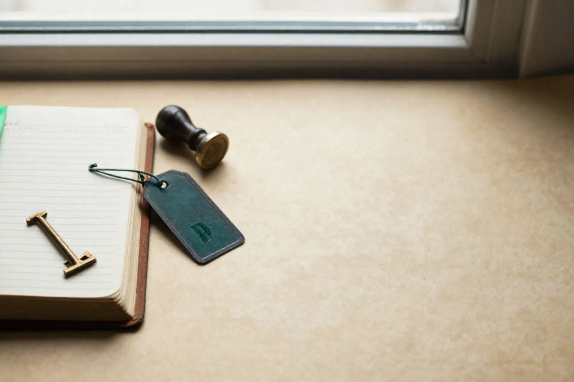 Open leather logbook with brass key, green silk ribbon, iron tags and rubber date stamp on ivory paper.