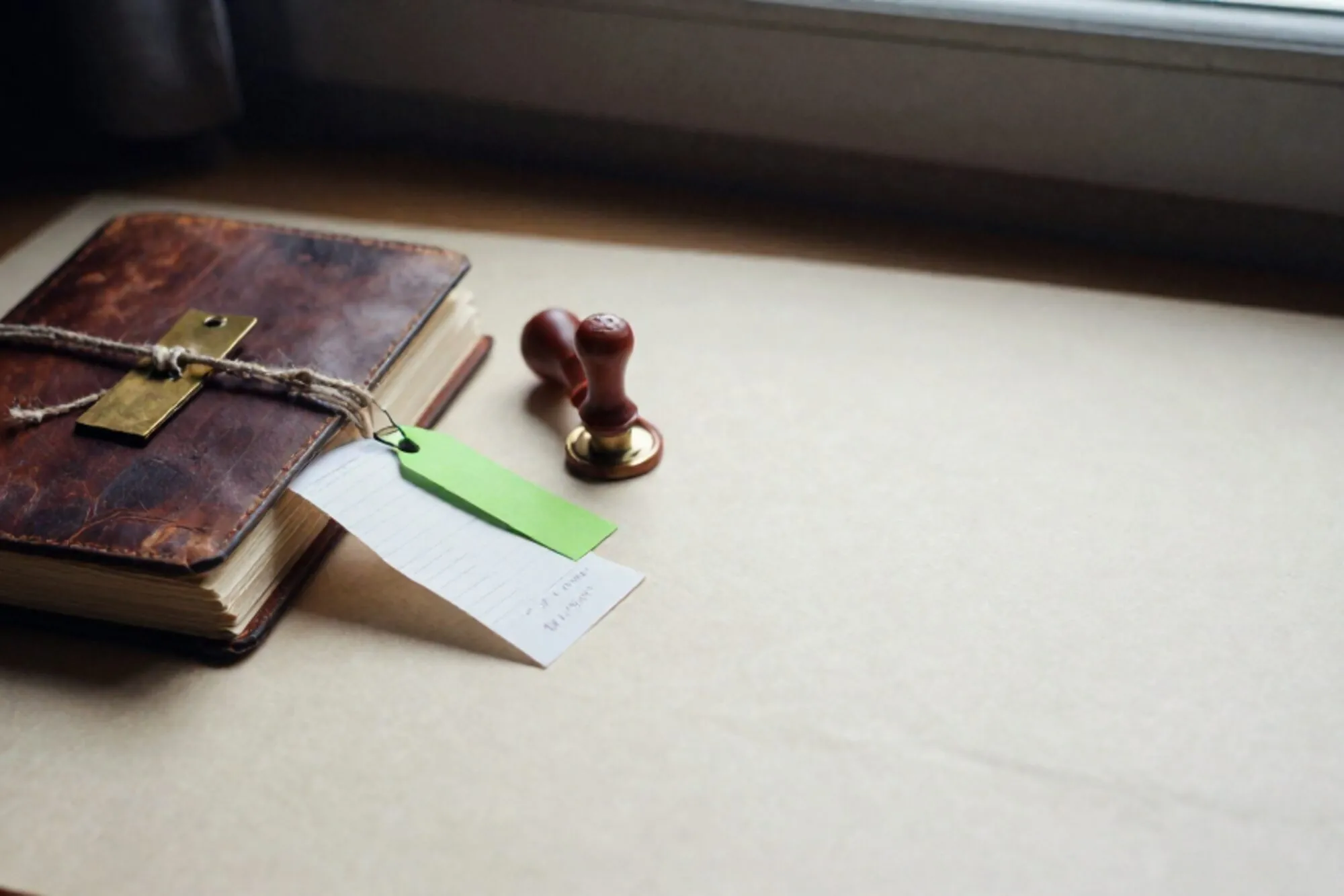 Open leather ledger on ivory desk, brass tags on linen twine, curled receipt with green price tag, red wax seal.