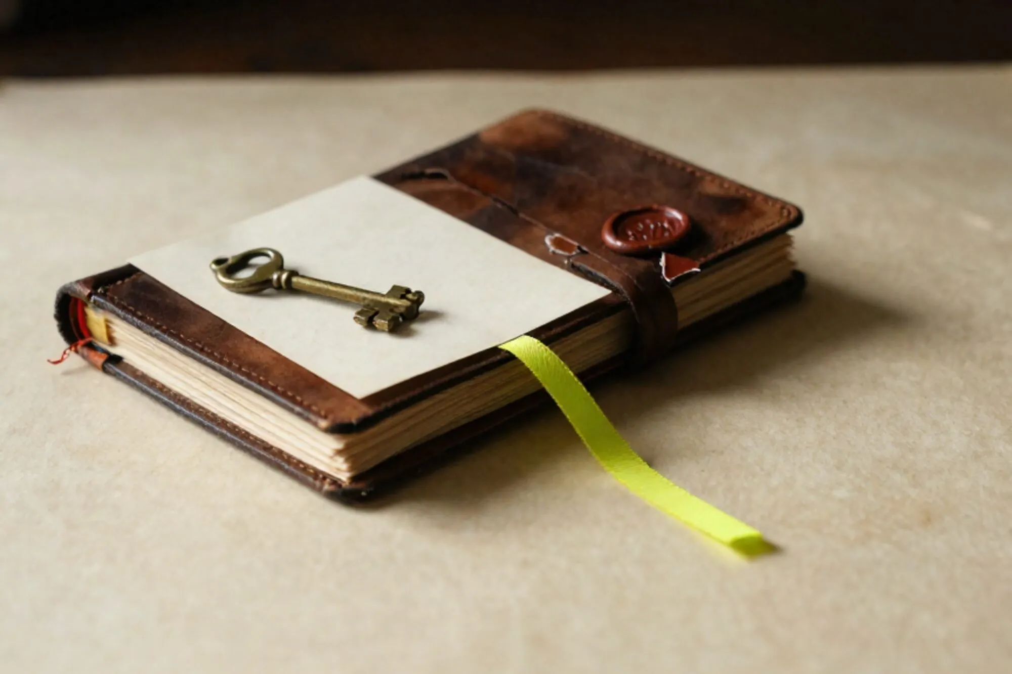 Leather ledger with shipping tags, brass key on cream card, green ribbon marker, broken red wax seal on ivory paper.