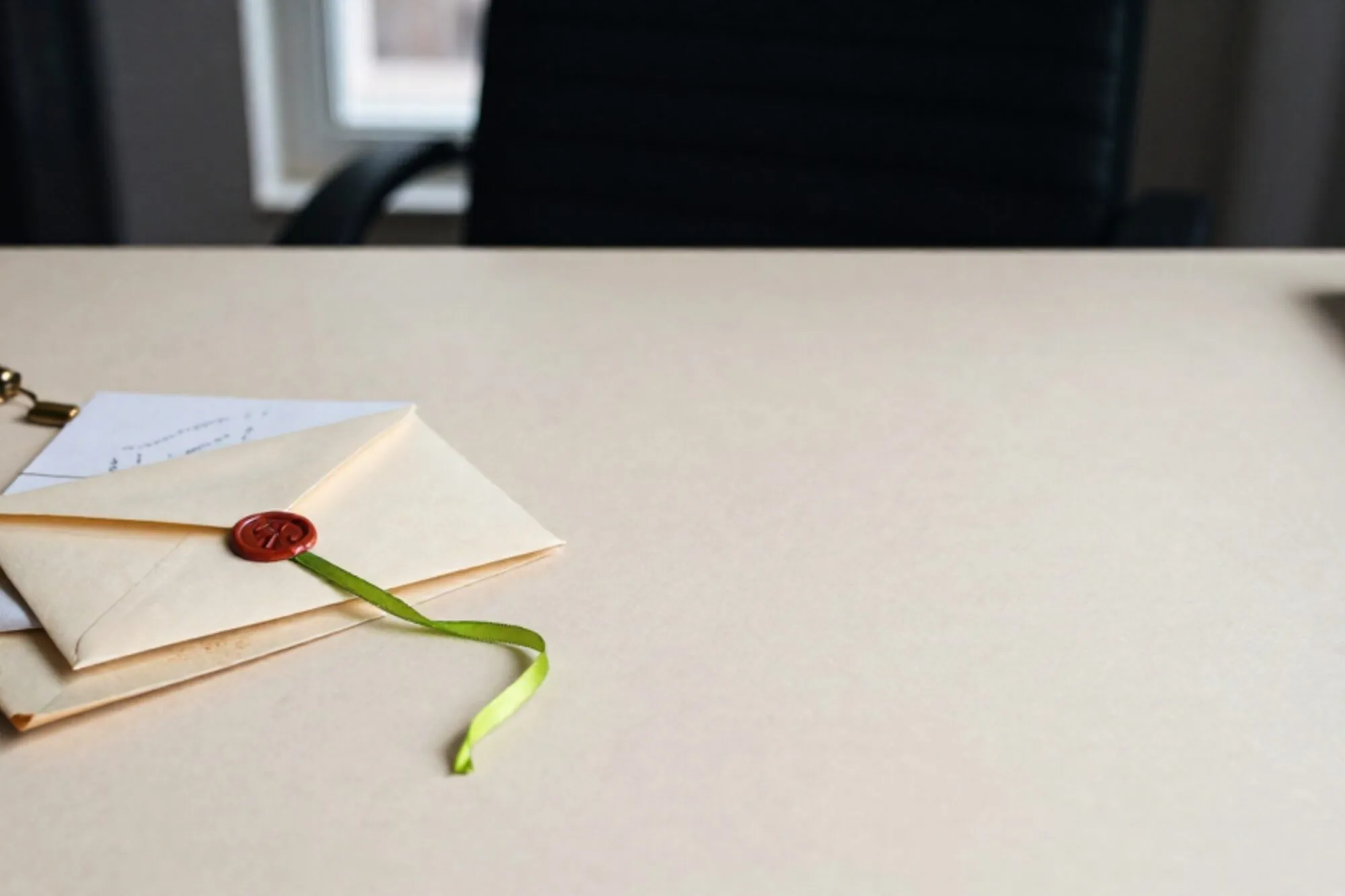 Cream wax-sealed envelope, brass letter-opener and carbon-copy slip on ivory desk, green ribbon trailing from flap.