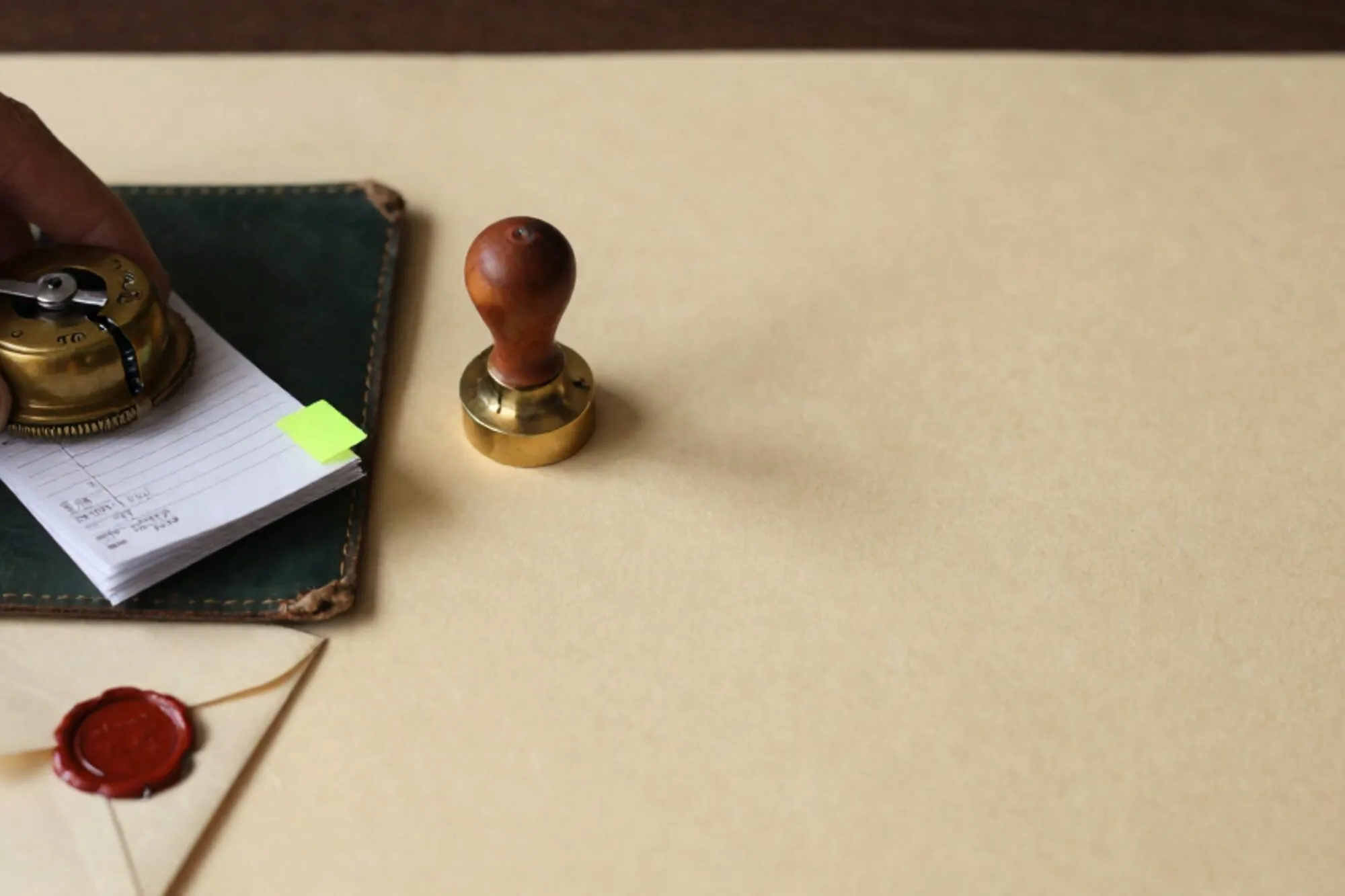 Ivory desk with leather blotter, brass tally counter, carbon receipts, green index tab, brass switch, broken wax seal.