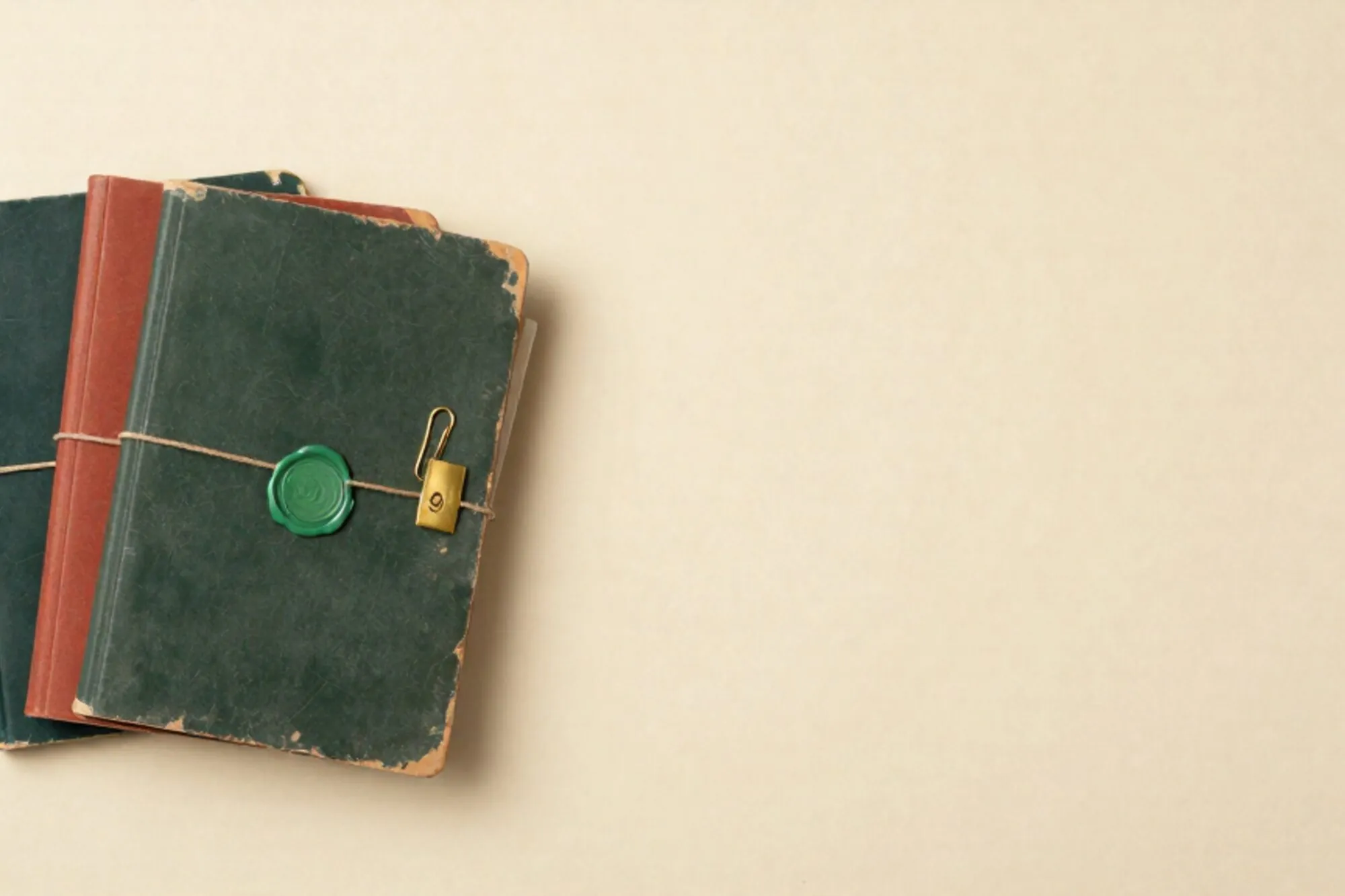 Three manila folders with coloured cords, brass tag, green wax seal, paperclip on ivory paper, window light.