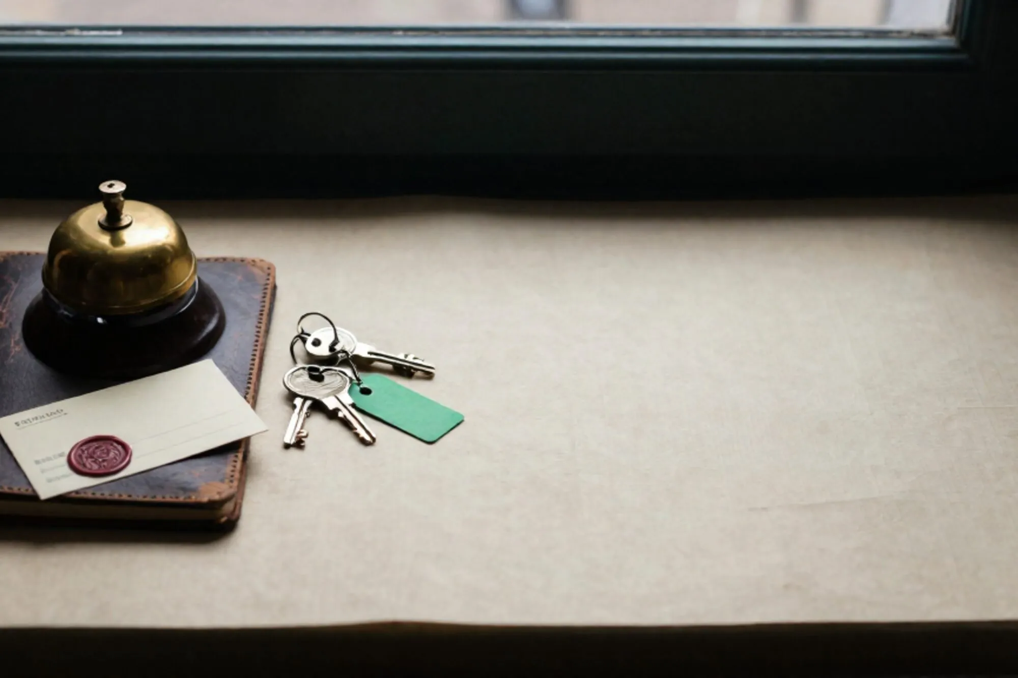 Brass hotel bell on leather ledger, three numbered key fobs, one with green tag, wax-sealed card, ivory linen.