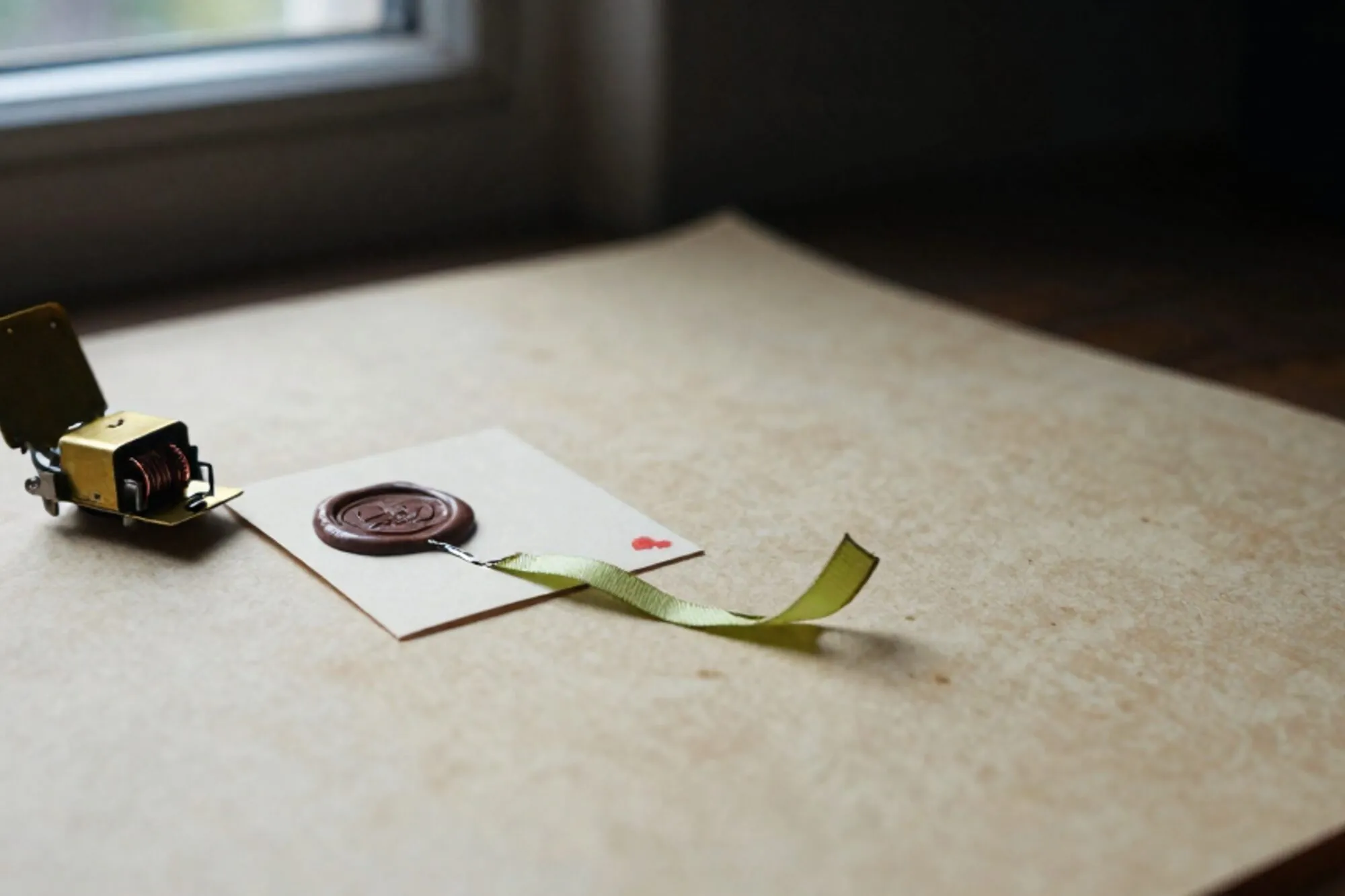 Brass relay switch and cream index card with sliced wax seal, green ribbon trailing across bone-paper desk.