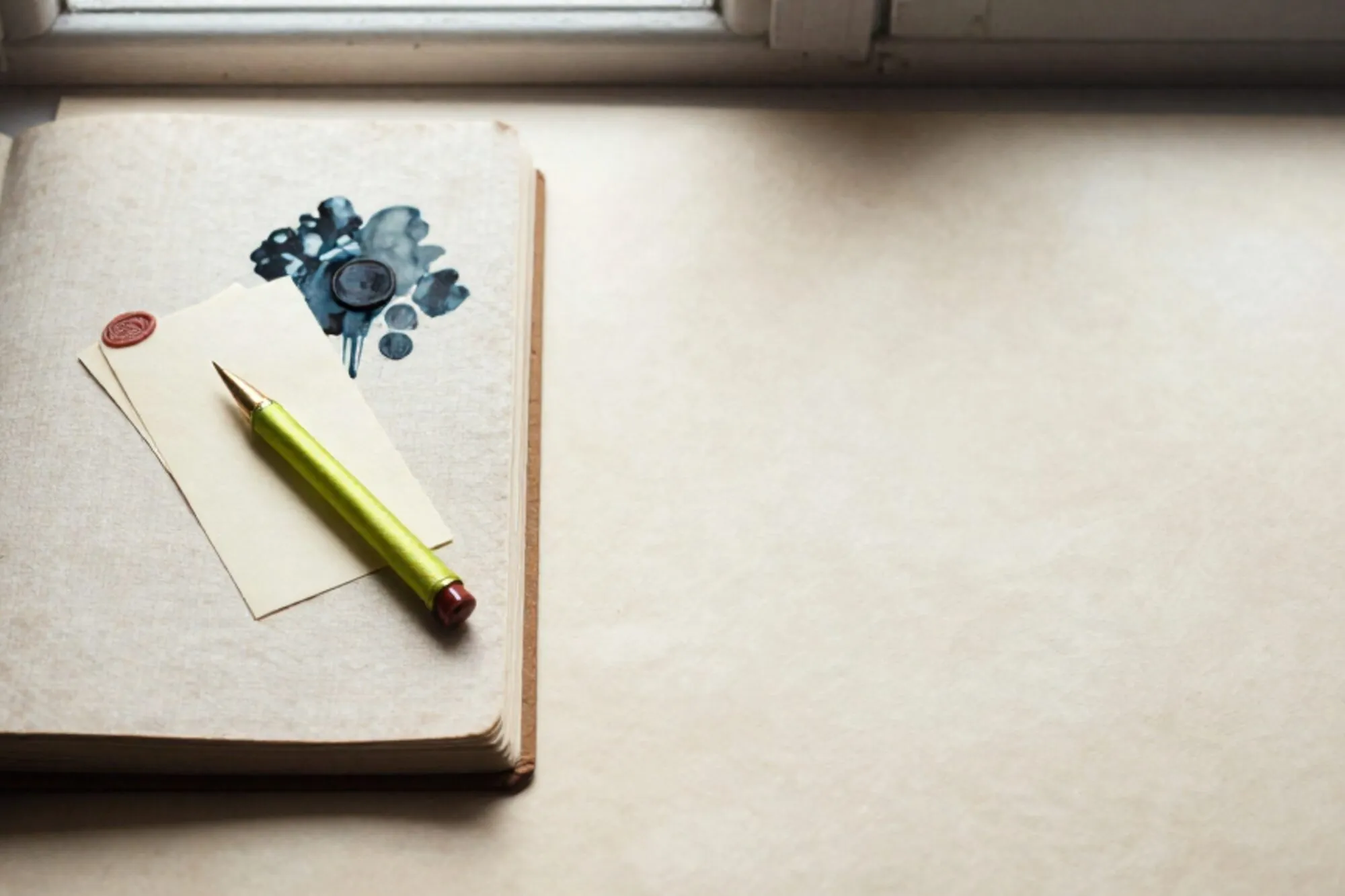 Open linen ledger on ivory paper, brass spike through cream slips, green ribbon, red wax seal.