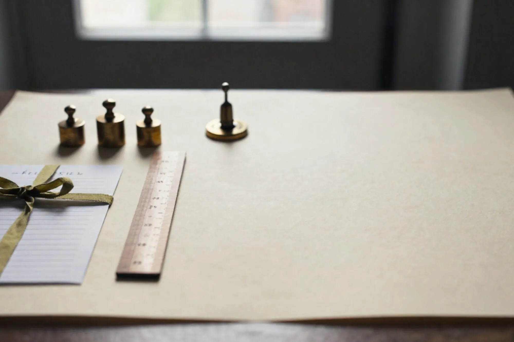Three brass weights, folded paper list with green ribbon, wooden ruler and brass relay on ivory paper.
