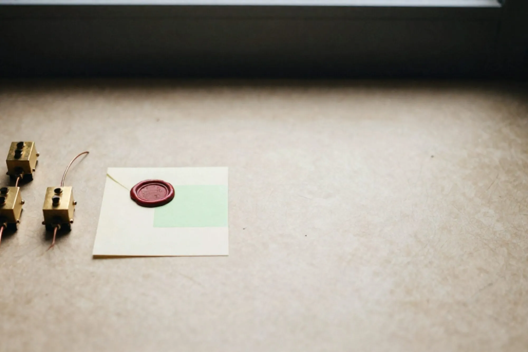 Three brass relays linked by copper wire on ivory paper, green sticky note and red wax seal, dark side light.