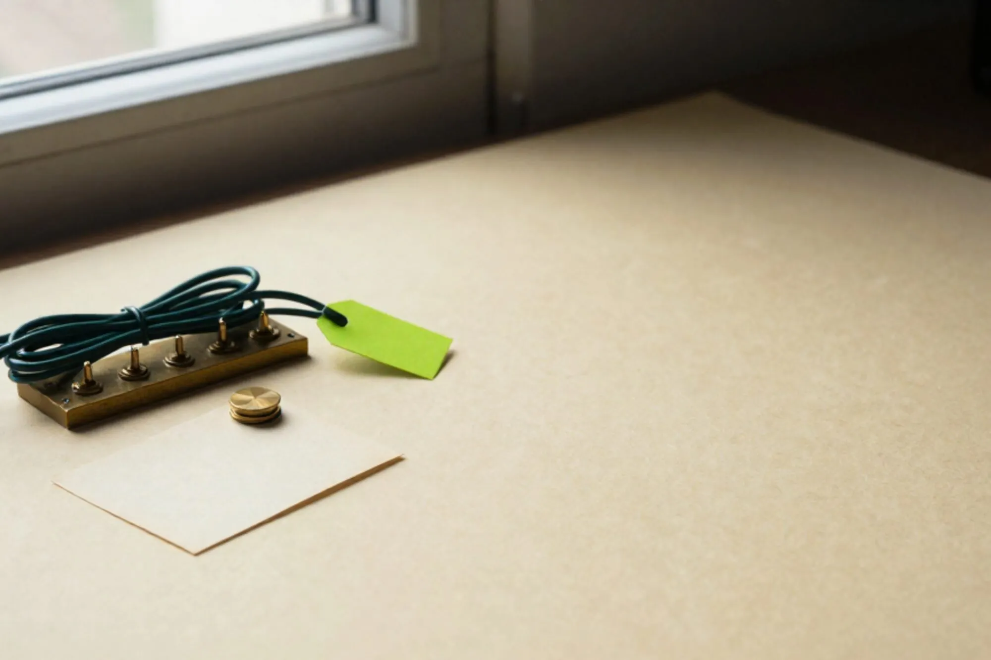 Brass switchboard with three green patch cables and a chartreuse paper tag on ivory paper, beside a cream index card.