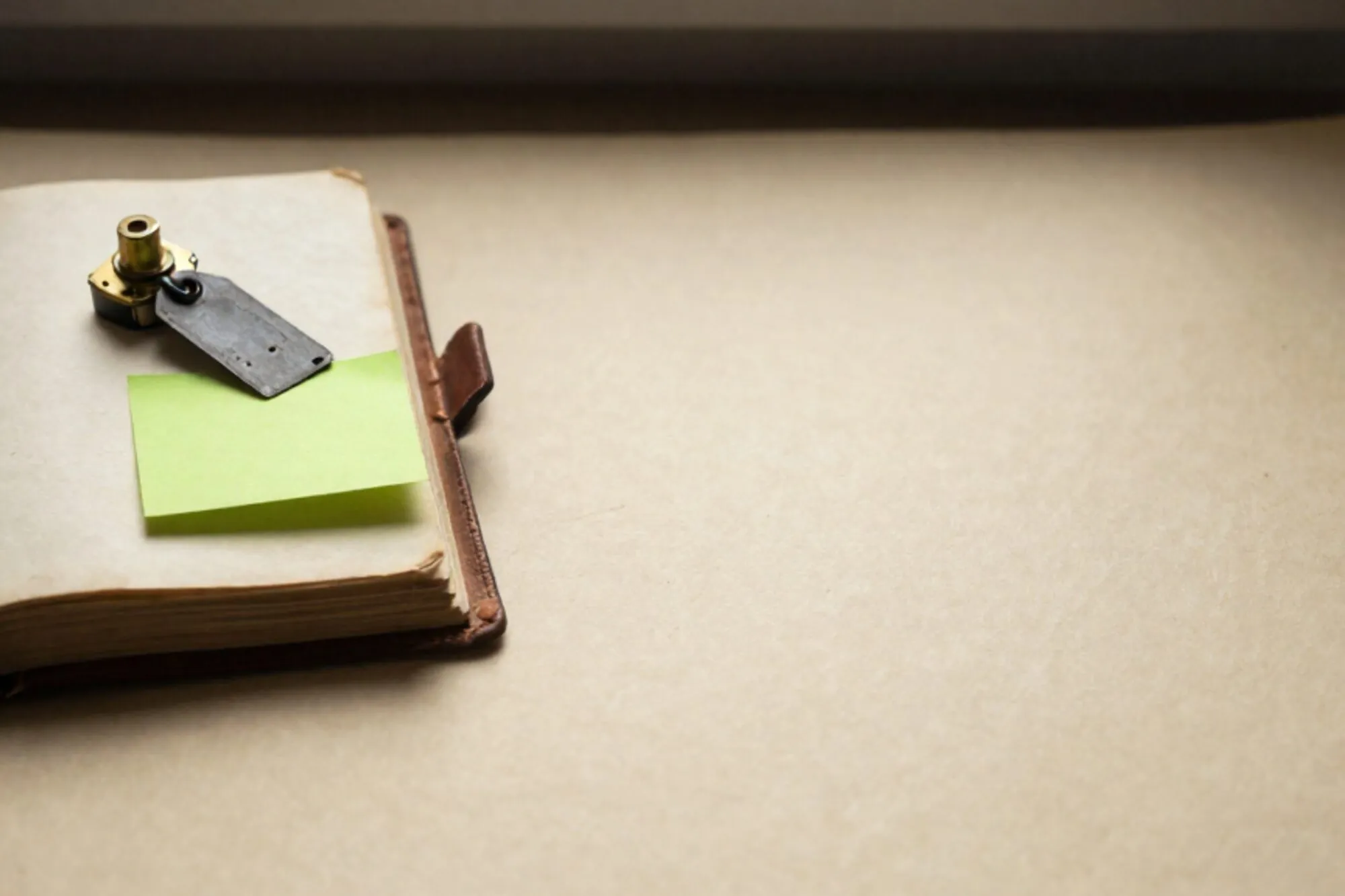 Open leather ledger on ivory paper with brass relay, iron tag, green sticky note, red wax fragment, side light.