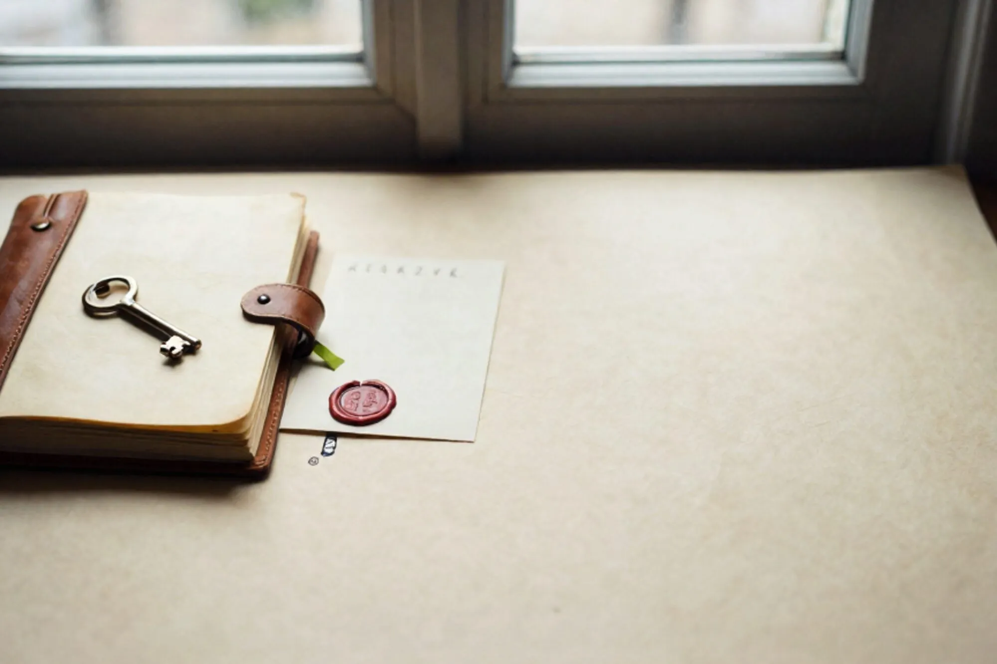 Leather logbook half-open with brass key on yellowed pages, cream index card, red wax seal, green ribbon on ivory paper.