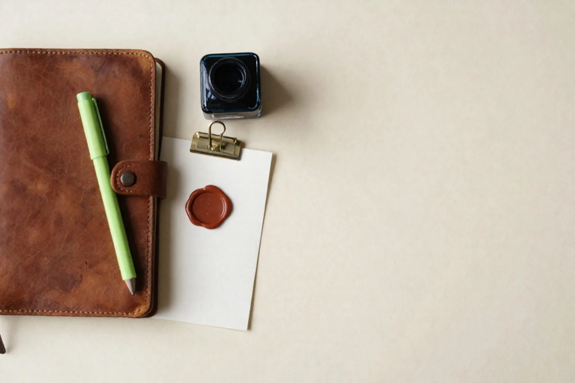 Gesloten leren logboek met groen lint, kaart met messing rand, lakzegel en inktkussen op ivoor papier.