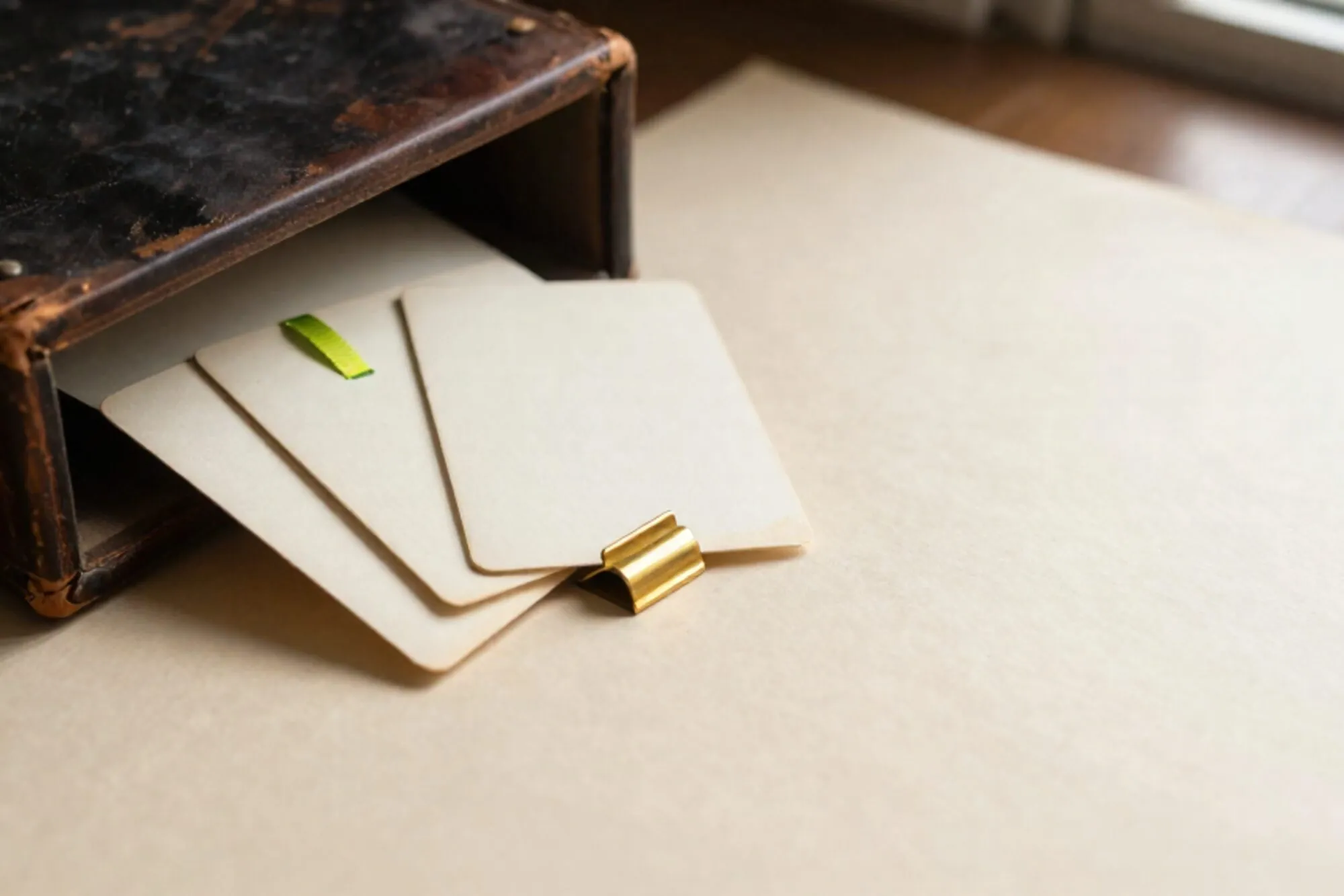 Half-open oak index card drawer with cream cards, brass tab, green ribbon, leather logbook on ivory desk.