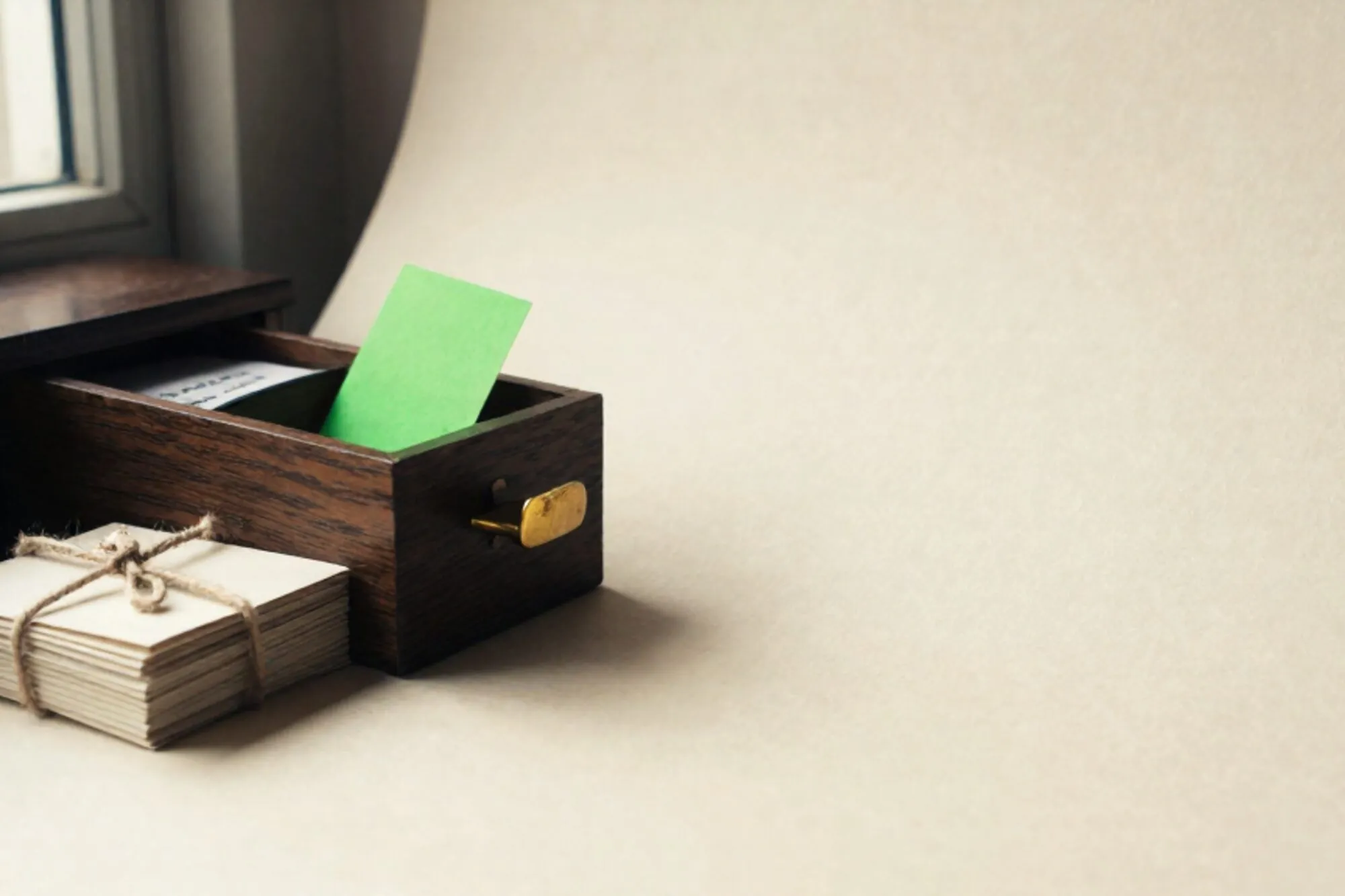 Open oak index-card drawer with one raised chartreuse card, brass divider, twine-tied cream cards on ivory paper.