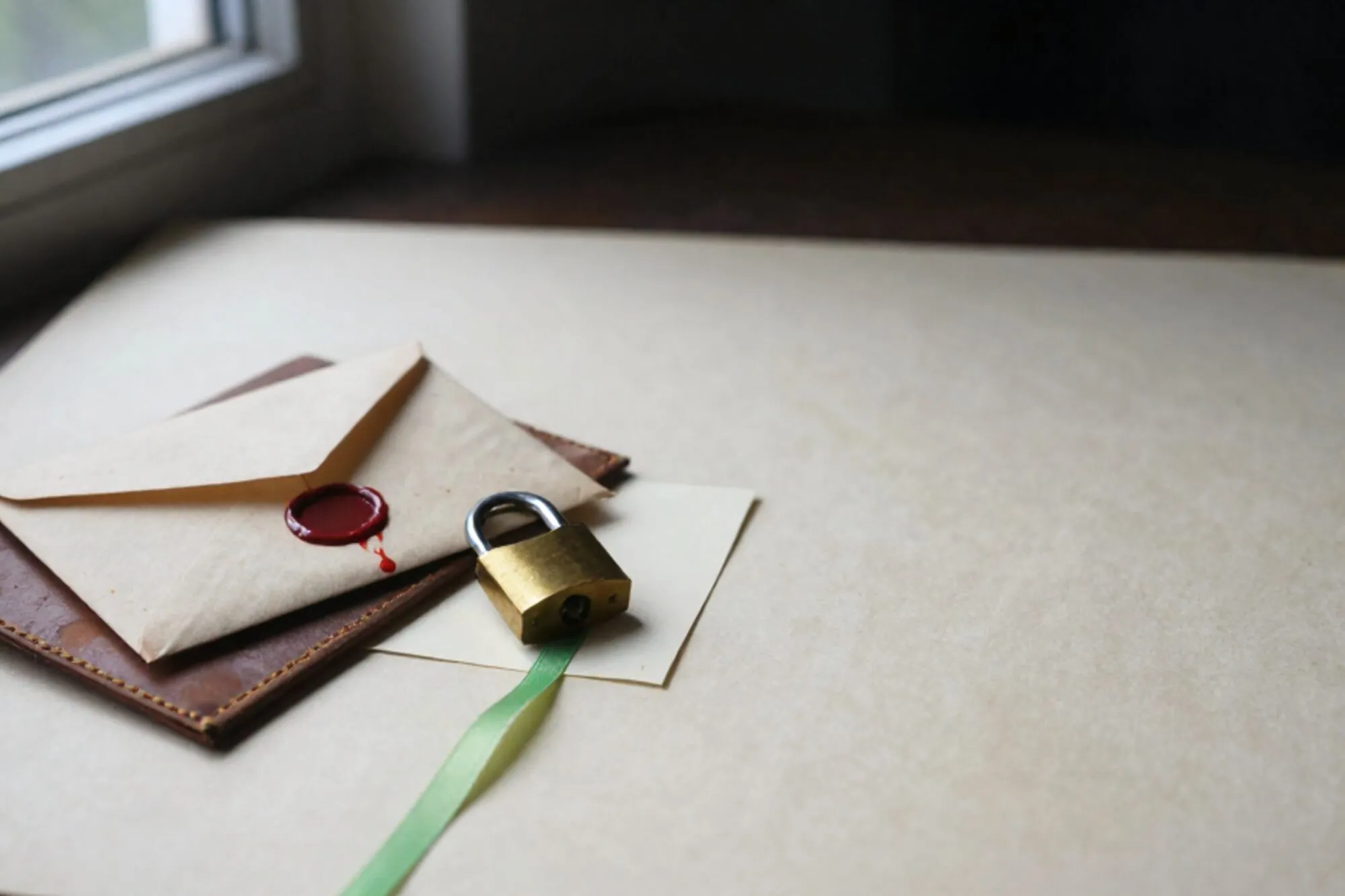 Manila envelop met gebroken lakzegel op leren onderlegger, groen lint, klein messing hangslot op crème indexkaart.