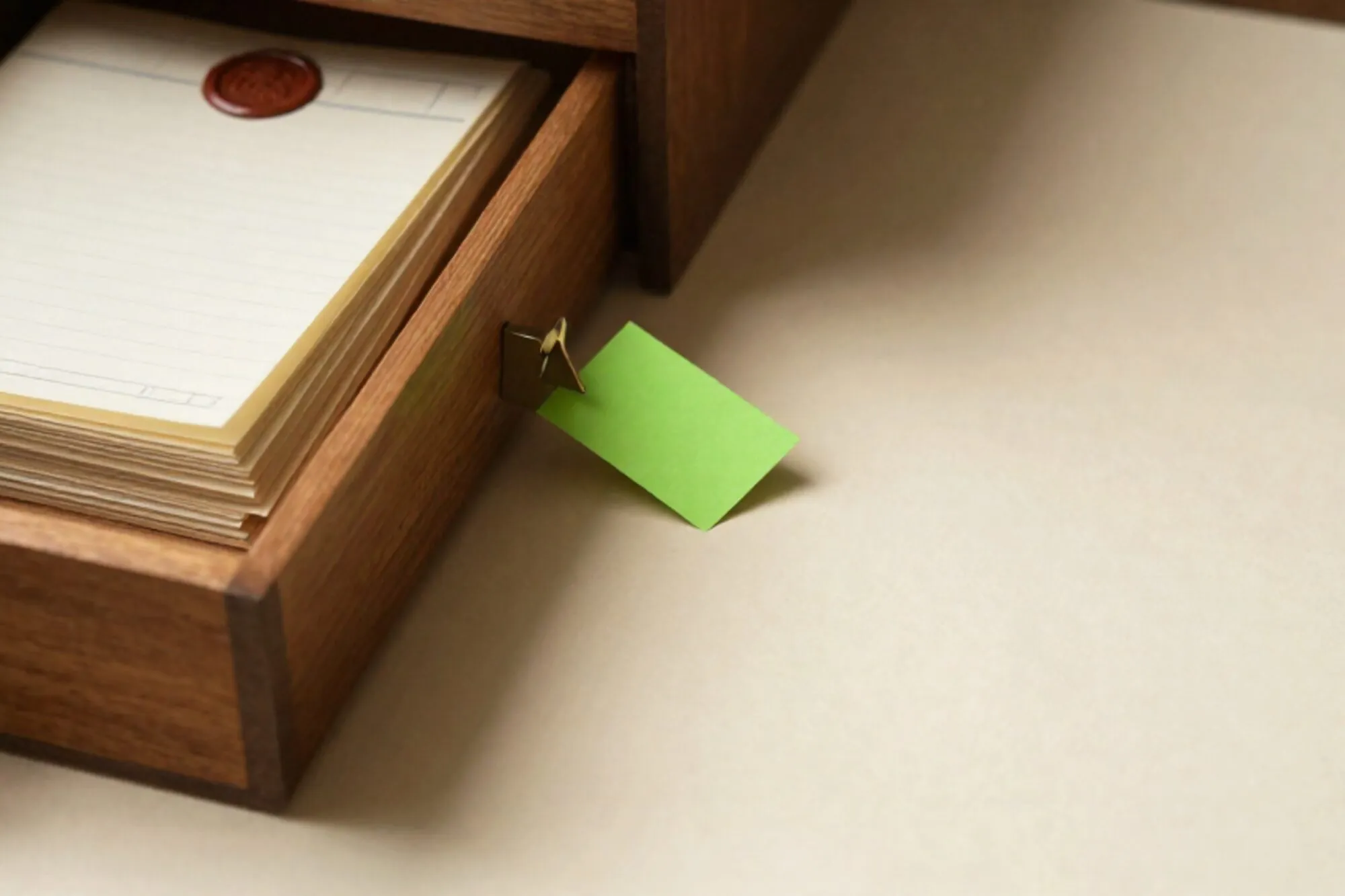 Open eiken kaartenbak met messing tussenschot, stapel crème grootboekpapier, groene tab, rode lakzegel op ivoor.