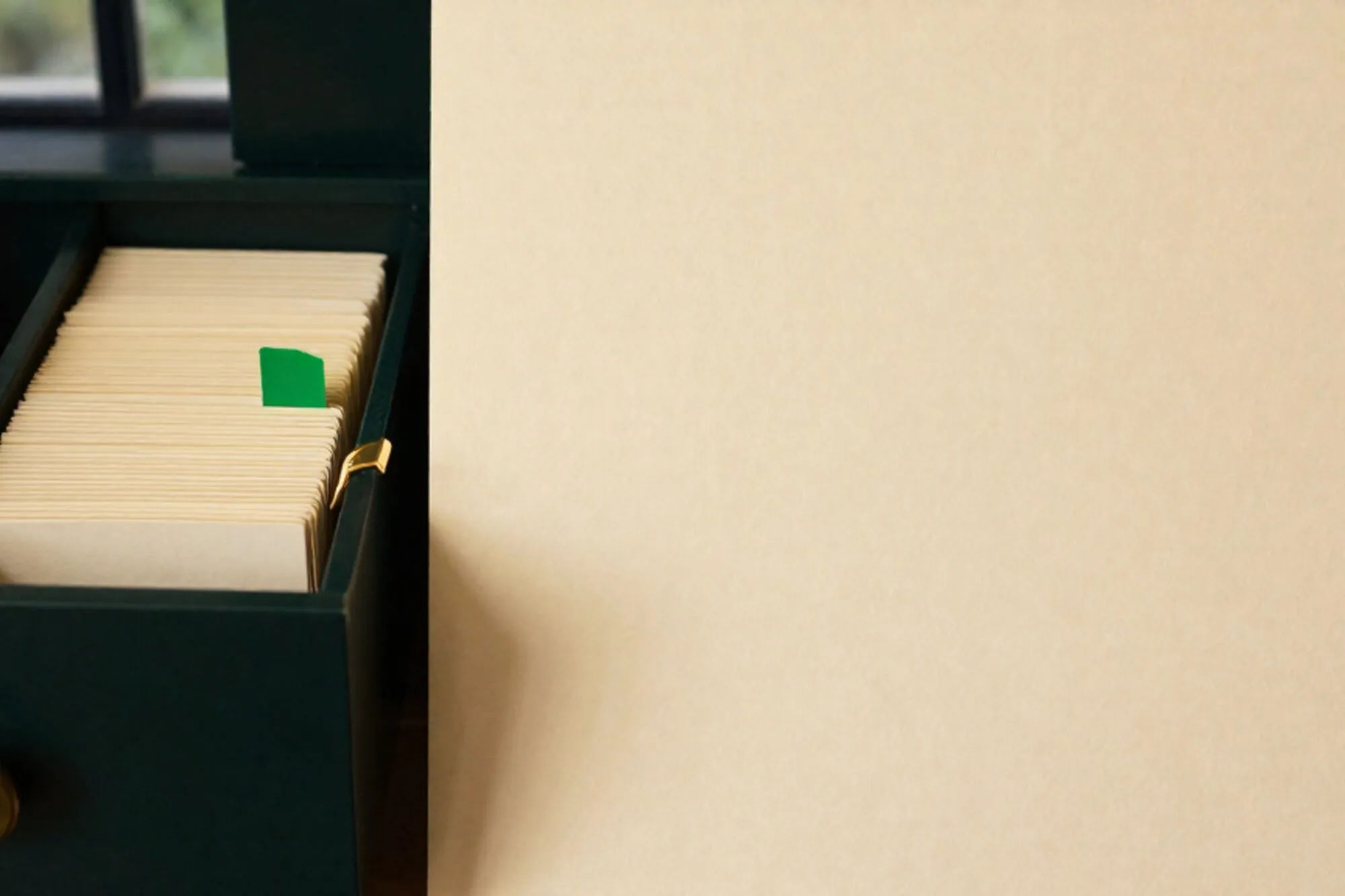 Open oak card-catalogue drawer with cream index cards, one chartreuse tab raised, brass divider, ivory paper surface.