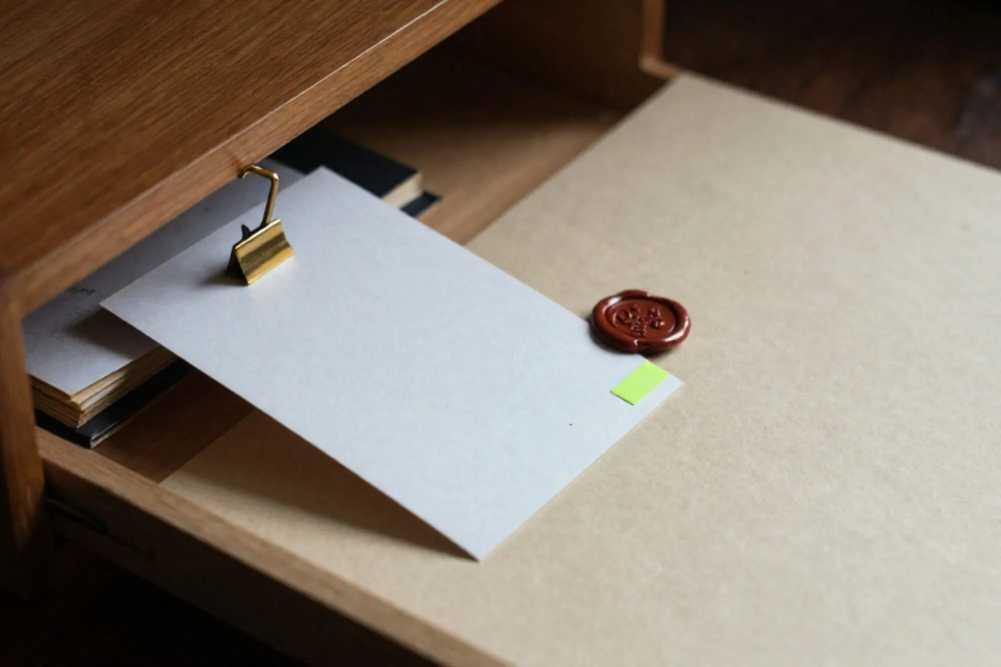 Open oak index-card drawer on ivory desk, one card tagged green, brass divider tilted, red wax seal fragment beside it.