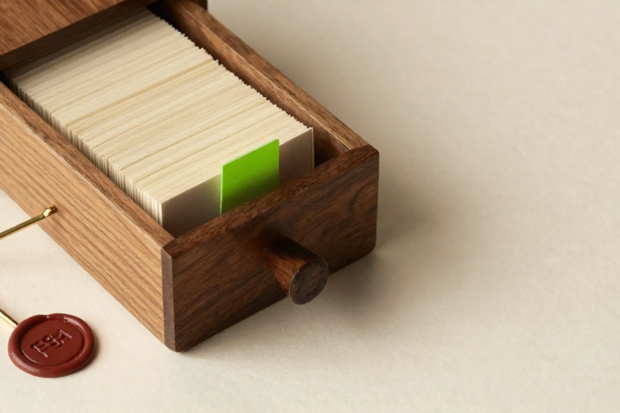 Houten kaartenbak open op ivoor papier, crème kaarten erin, één limegroen tabblad omhoog, messing tussenschot, rode lakzegel.