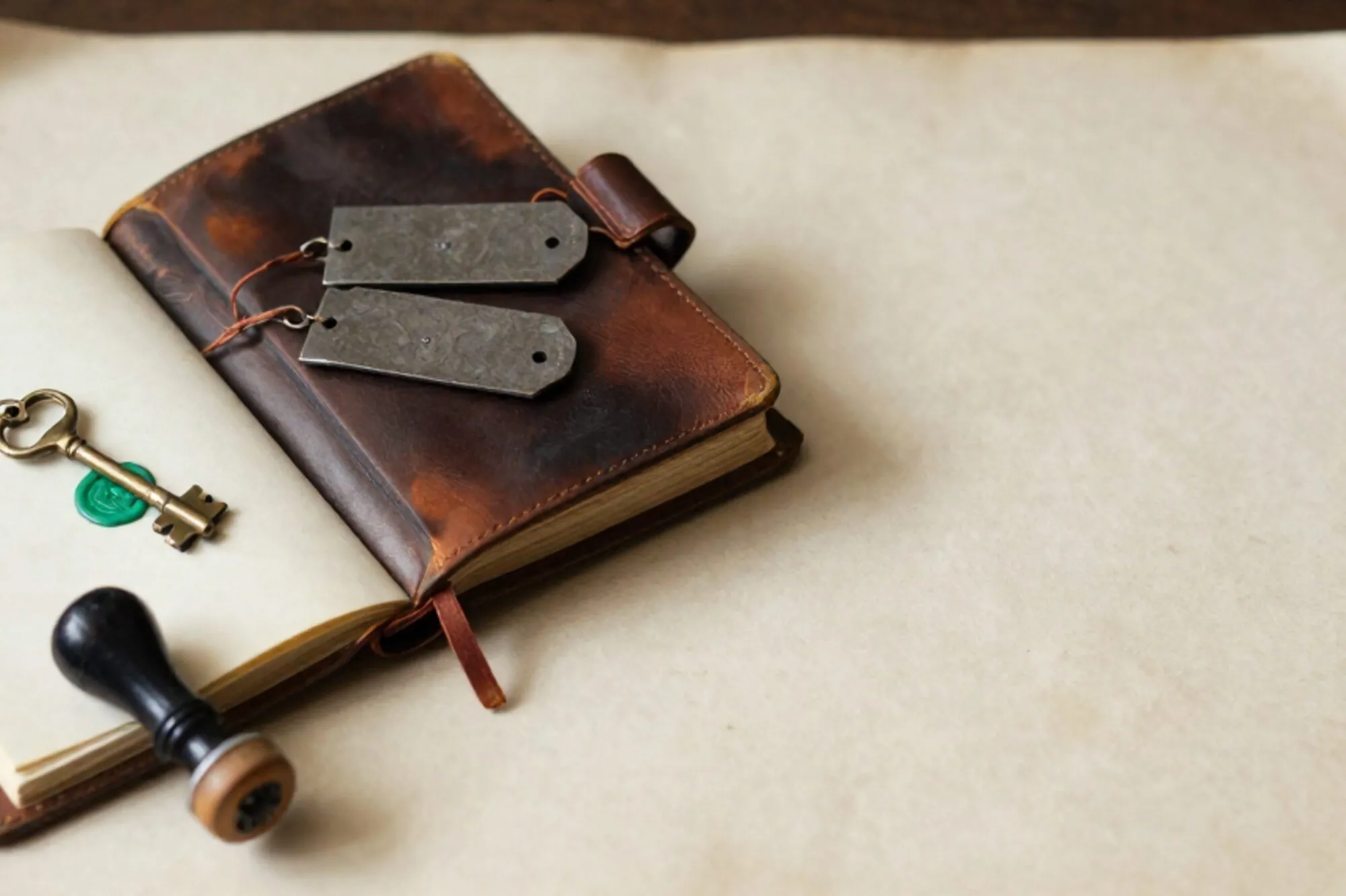 Open leather logbook with iron shipping tags, brass key on index card with green wax seal, ink pad and stamp on ivory paper.