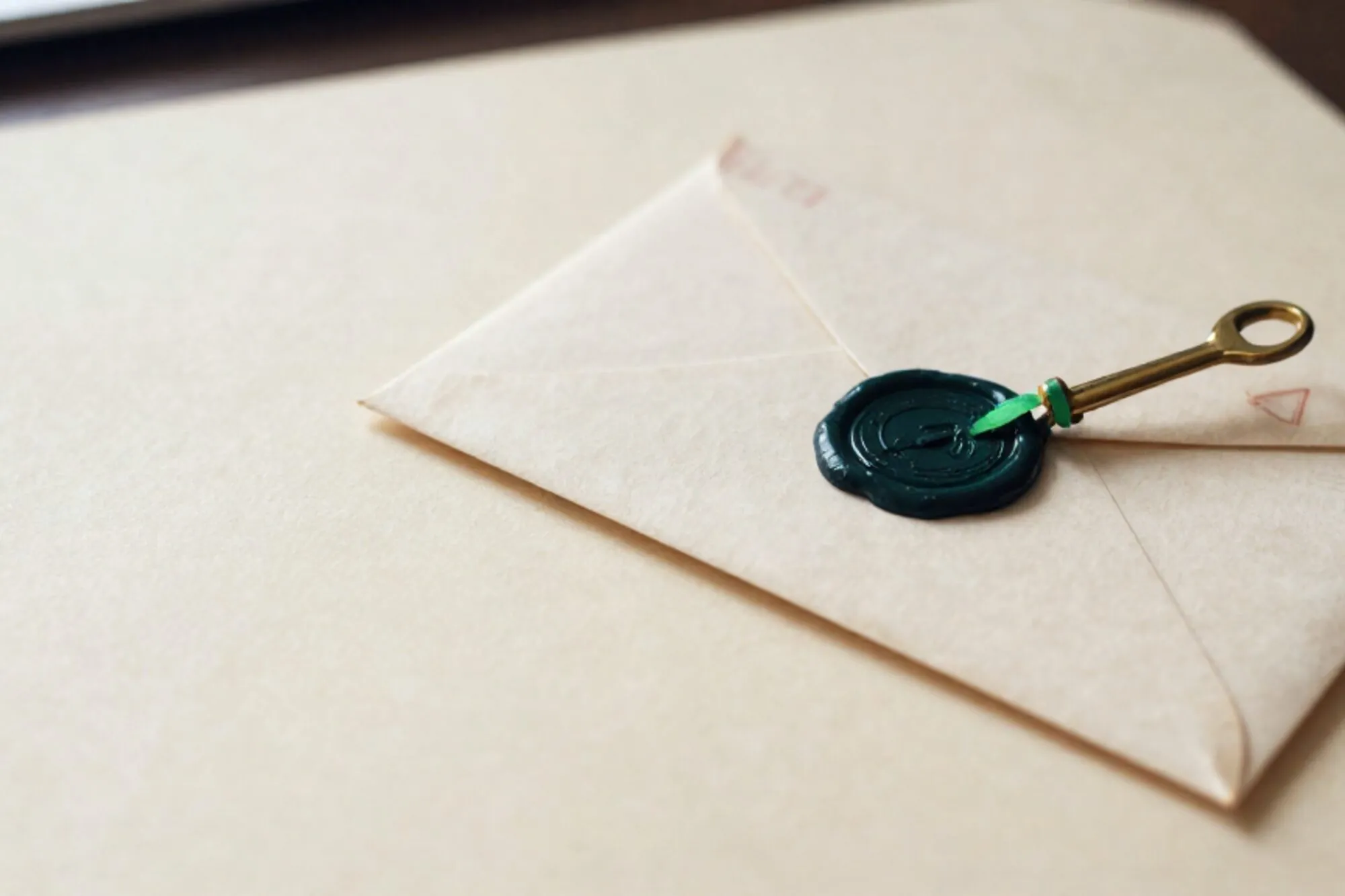 Crème envelop met groen lakzegel, messing briefopener, groen lint en rode postzegel op ivoorpapier.